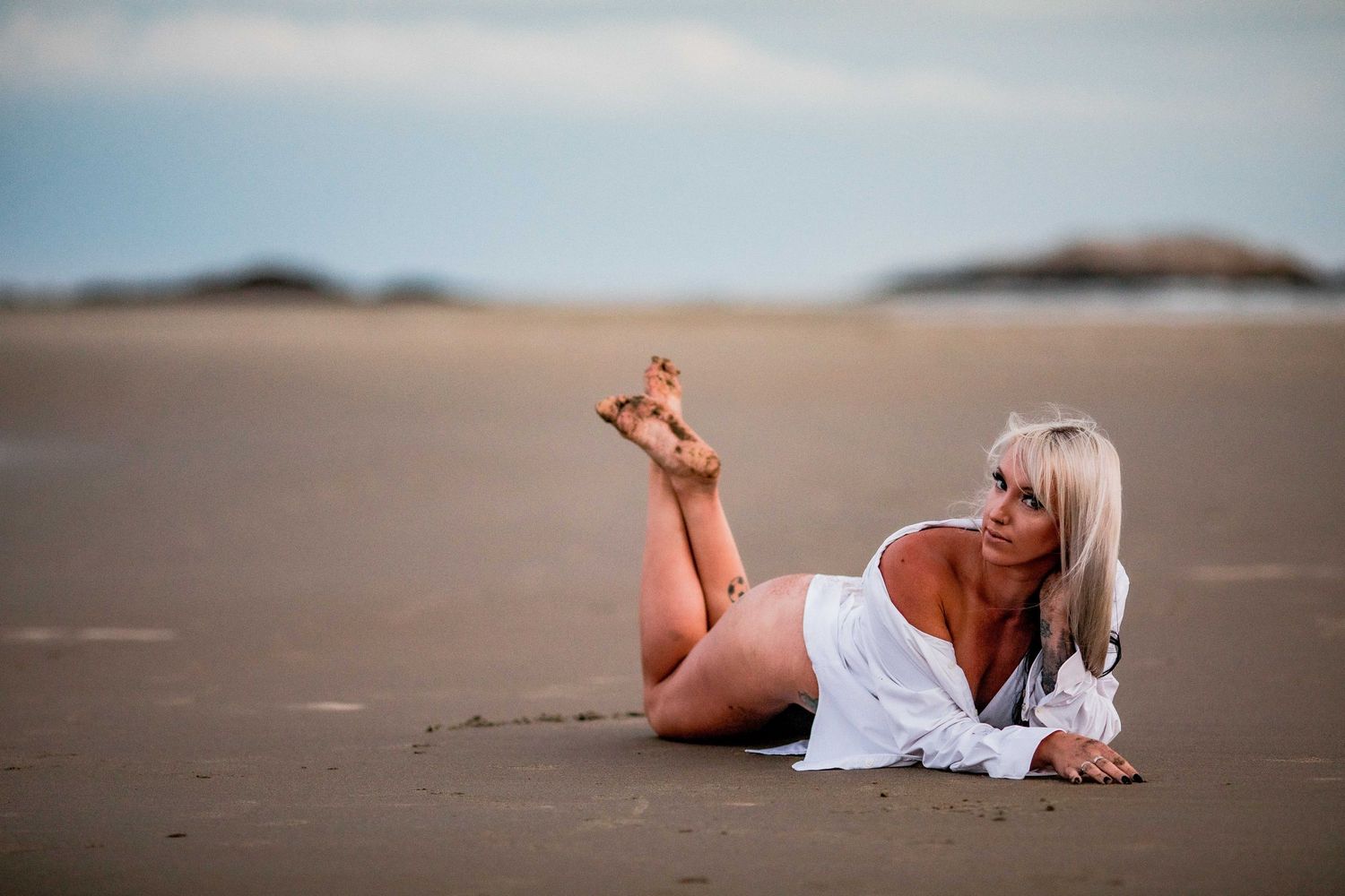 Blonde woman in white shirt lying on sandy beach posing at dusk. Cape cod beach Boudoir photos