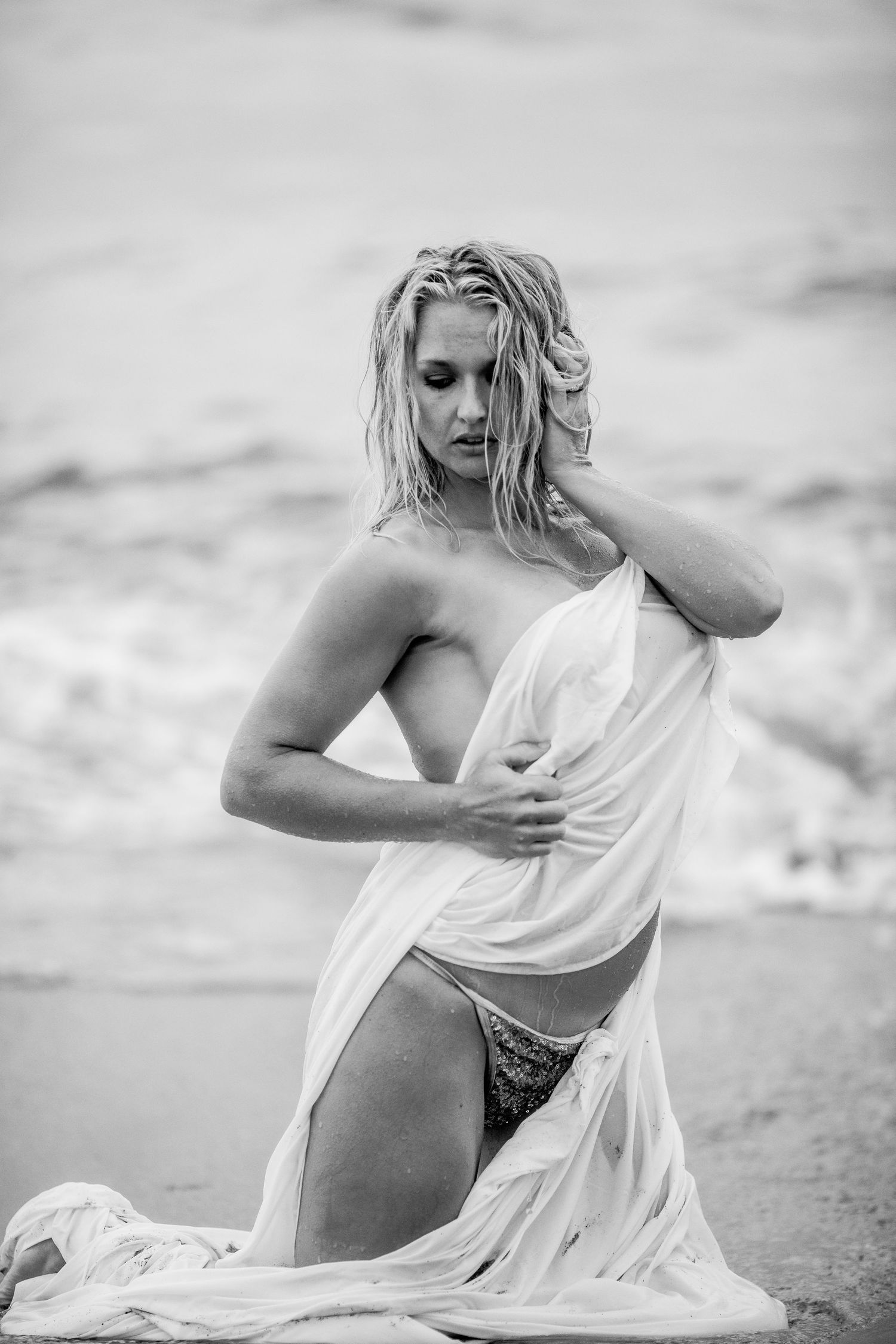 Black and white artistic photo of a wet blonde woman on beach holding white fabric Cape cod couples studio Boudoir photos