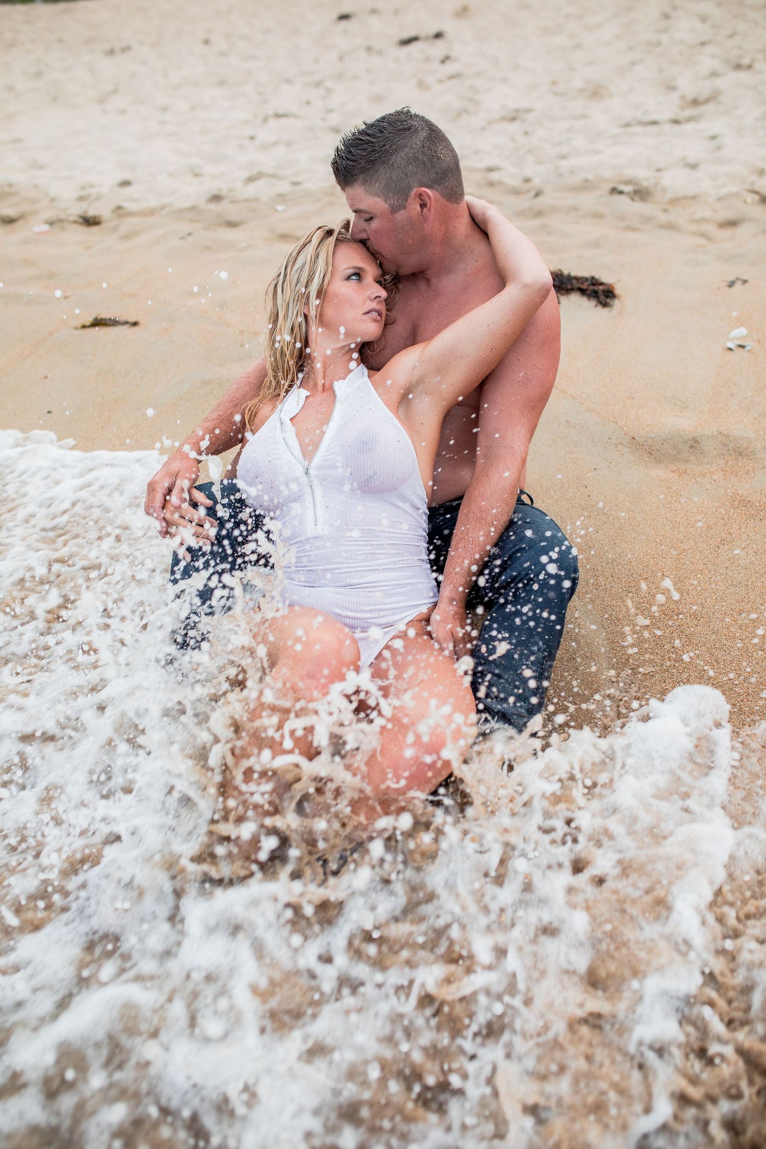 Romantic couple embracing and kissing while sitting together in splashing ocean waves on beach Cape cod couples beach Boudoir photos