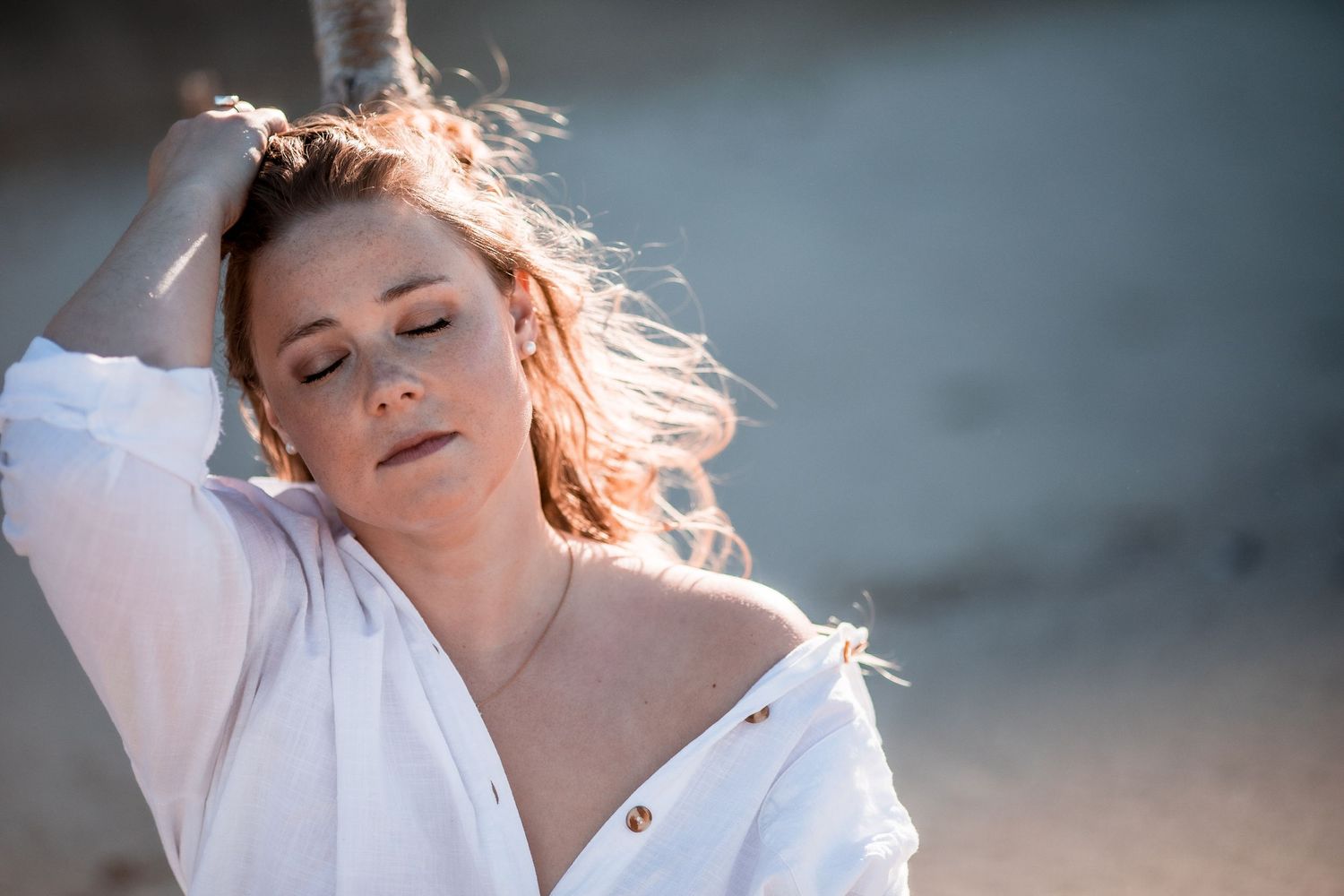 Redhead woman in white shirt with wind-blown hair posing outdoors in soft sunlight. Cape cod beach Boudoir photos