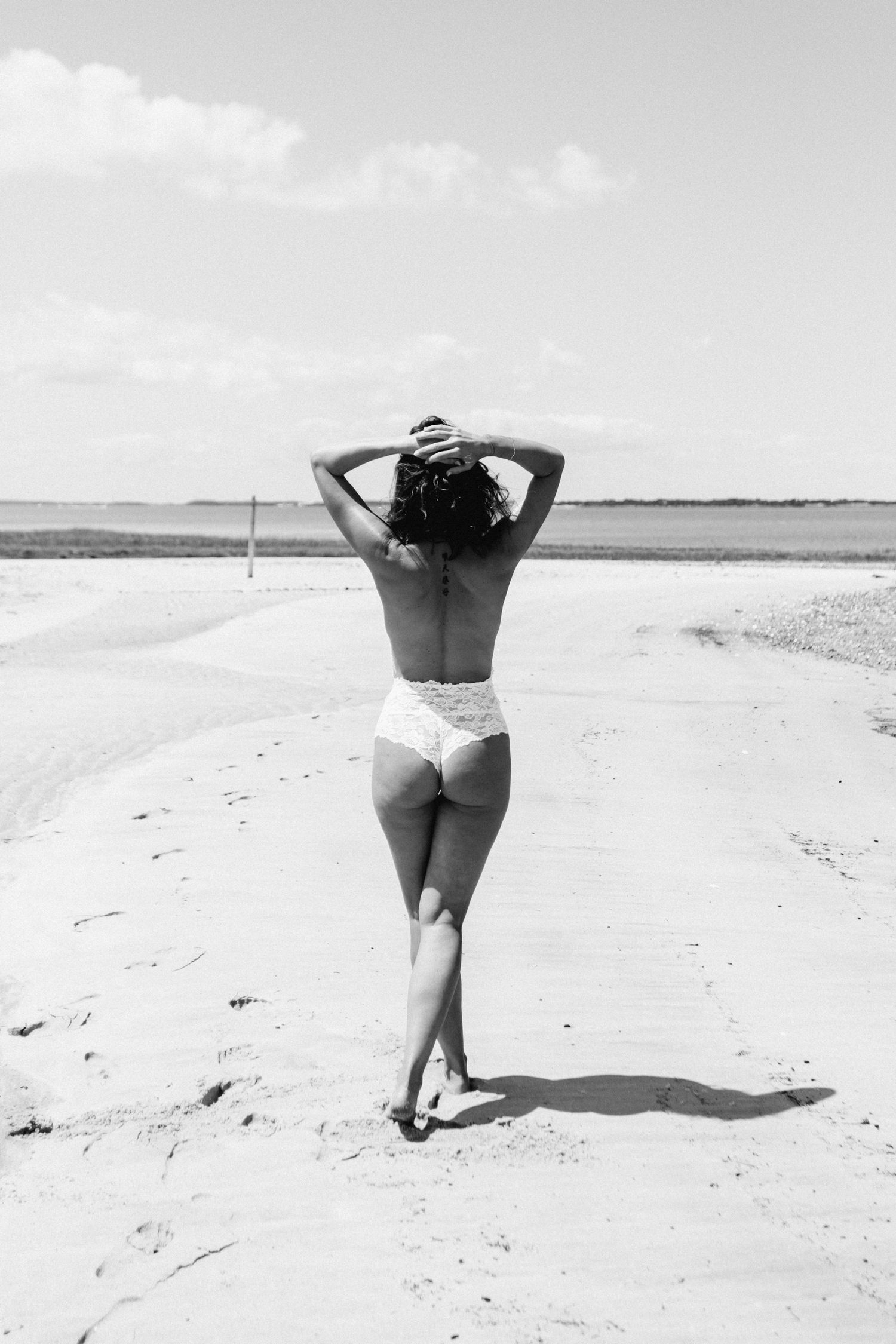 Black and white artistic photo of woman in white bikini walking on sandy beach road. Cape cod beach Boudoir photos