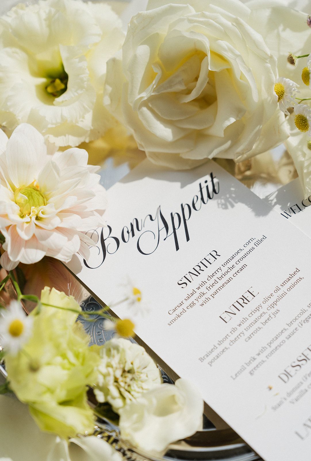 Elegant wedding menu card reading Bon Appetit surrounded by white roses, dahlias, and lisianthus flowers.