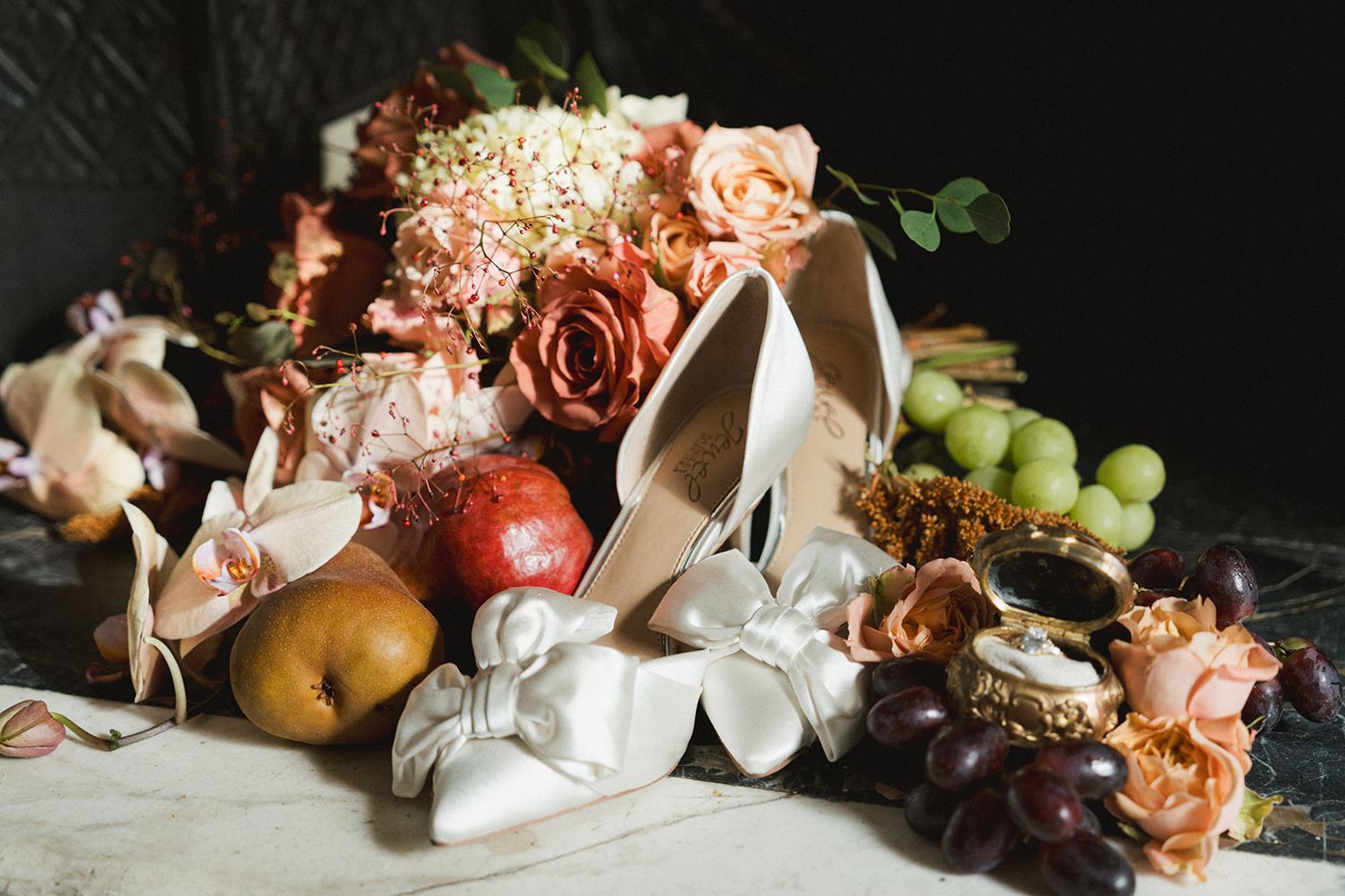 Bridal flat lay featuring white heels, blush roses, grapes, pears, and vintage accessories.