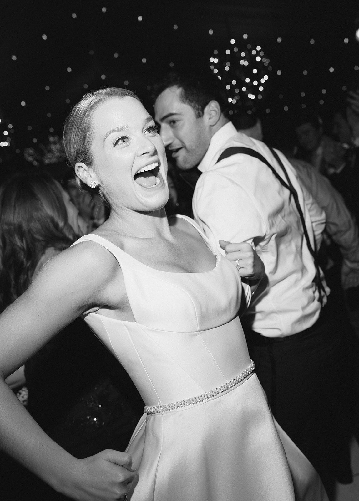 Joyful bride laughing on dance floor with groom in black and white candid wedding reception photo.