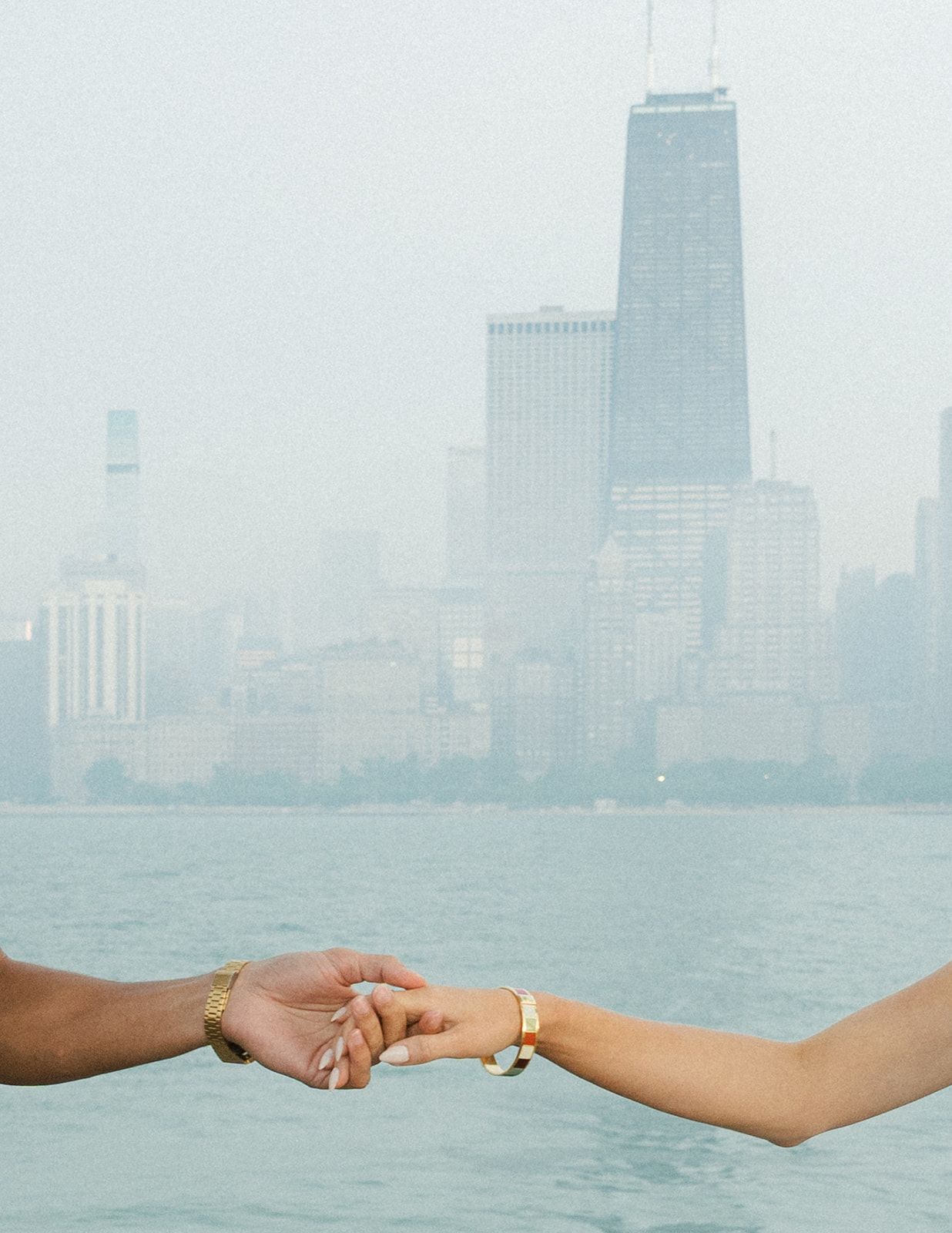 Two hands reaching toward each other over water with hazy Chicago skyline in the background.