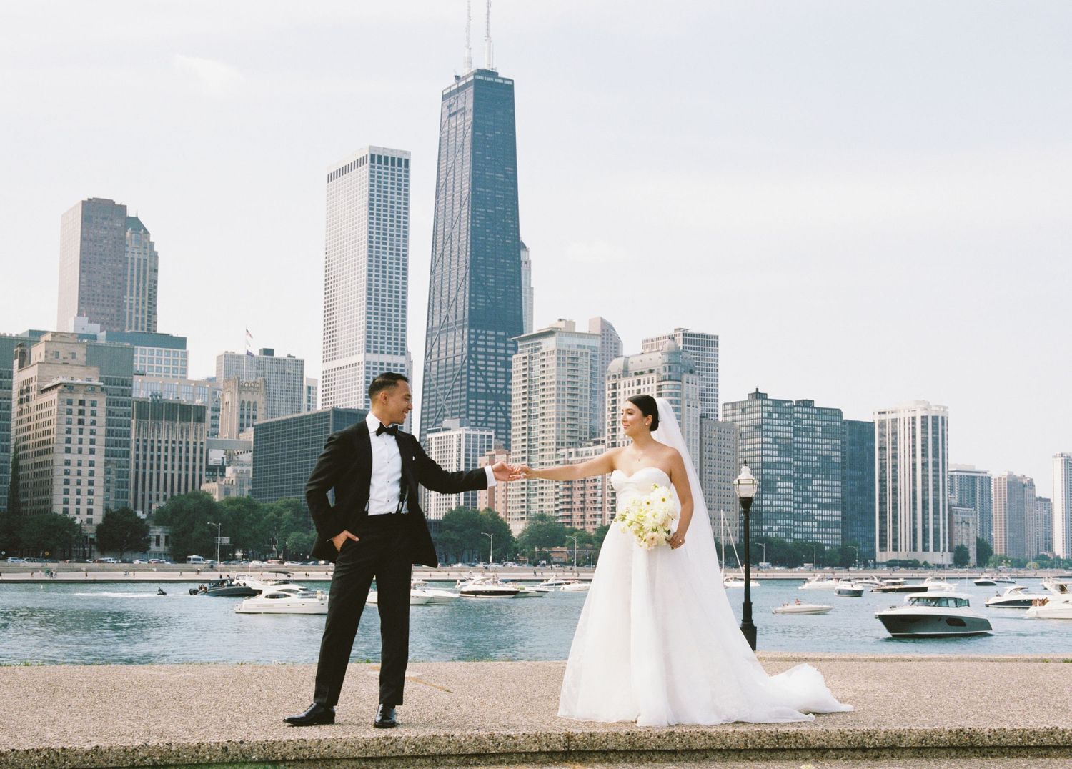 Bride and groom hold hands facing each other with Chicago skyline and Lake Michigan in the background.