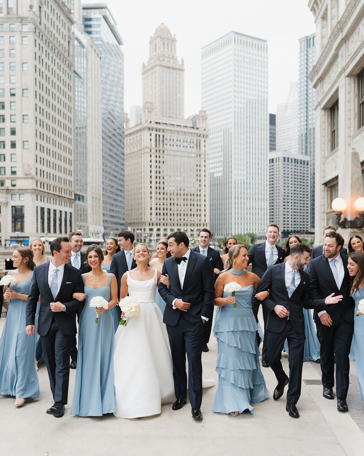 Wedding party in navy suits and blue gowns walking together with Chicago skyline in the background.