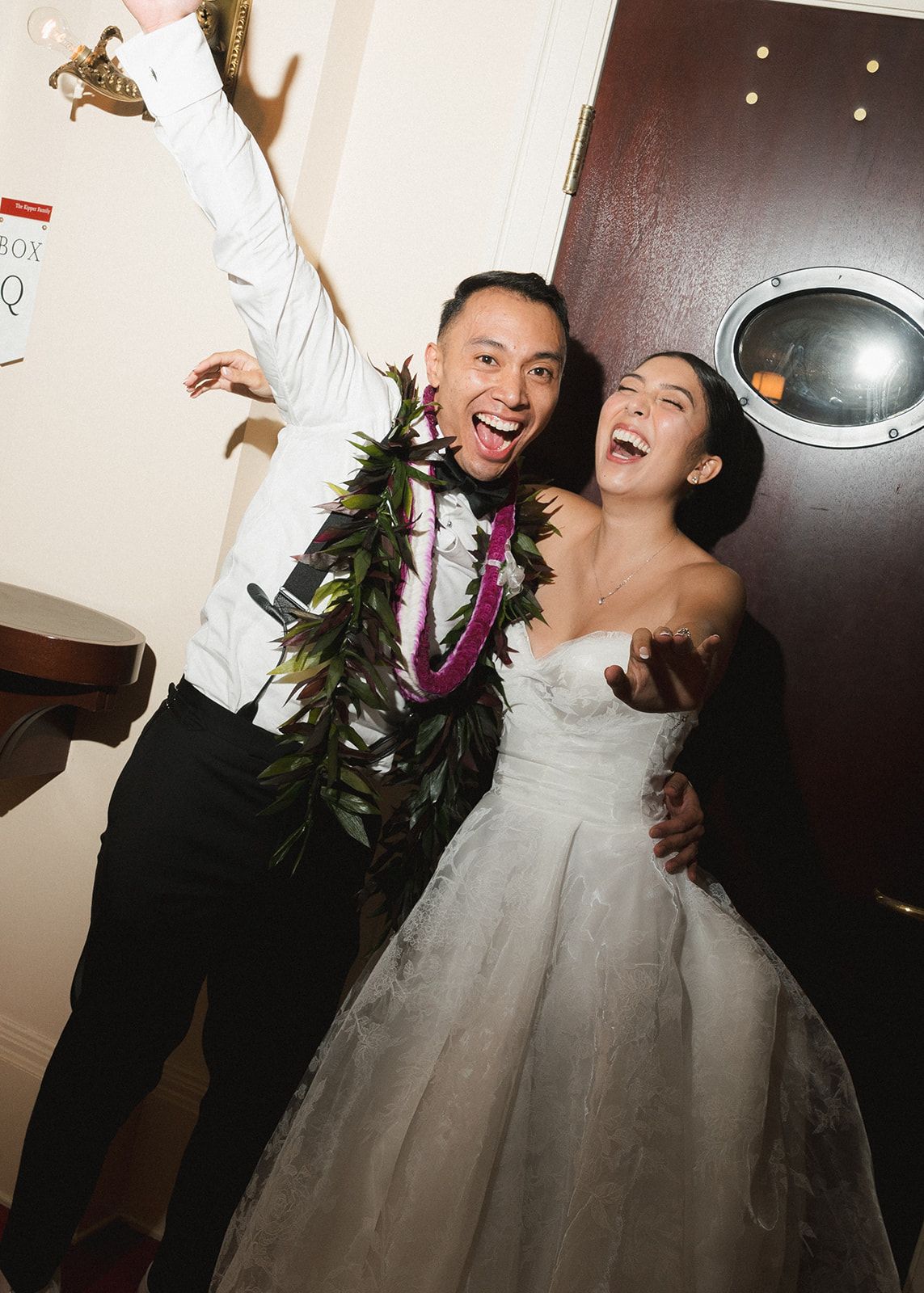 Joyful newlyweds celebrate wearing traditional Hawaiian lei garlands at elegant wedding reception venue.