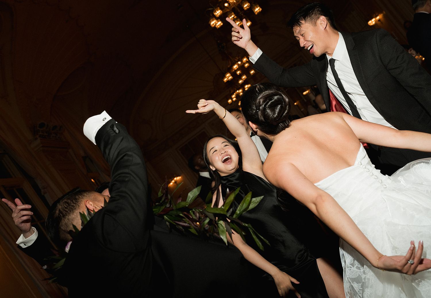 Joyful bride in white dress dancing energetically with guests in formal attire at elegant wedding reception.