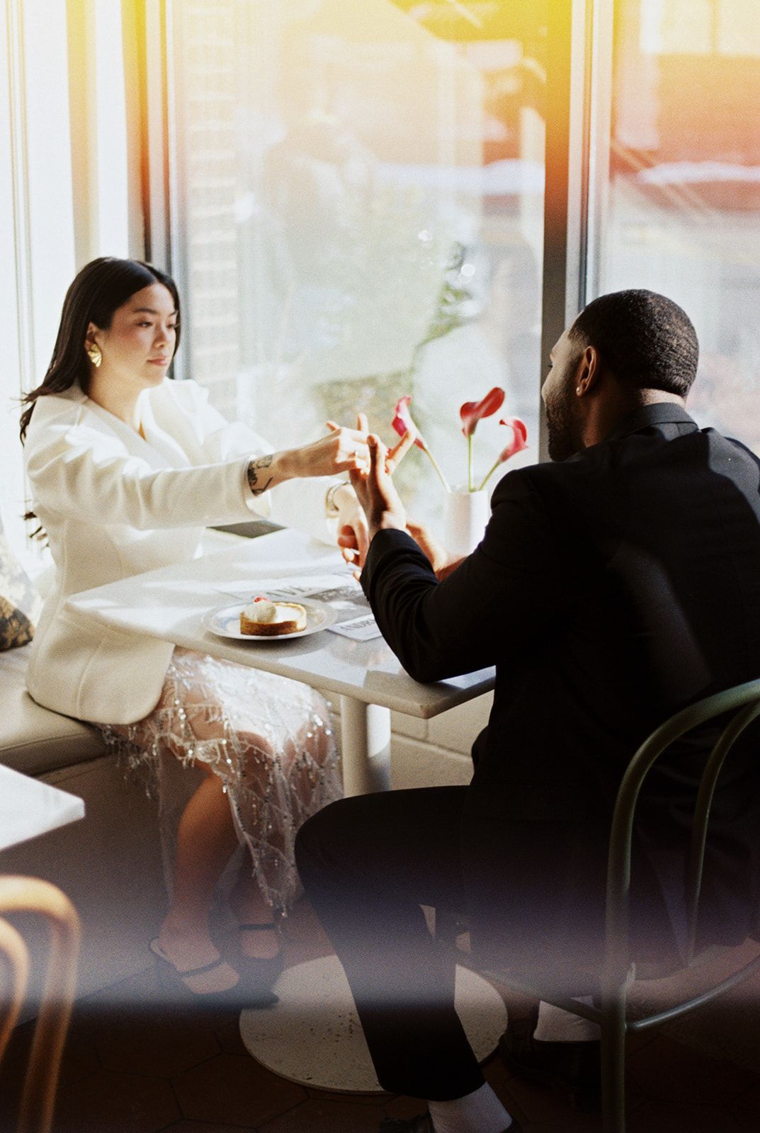 Interracial couple sitting at cafe table by window, exchanging save the date wedding cards.