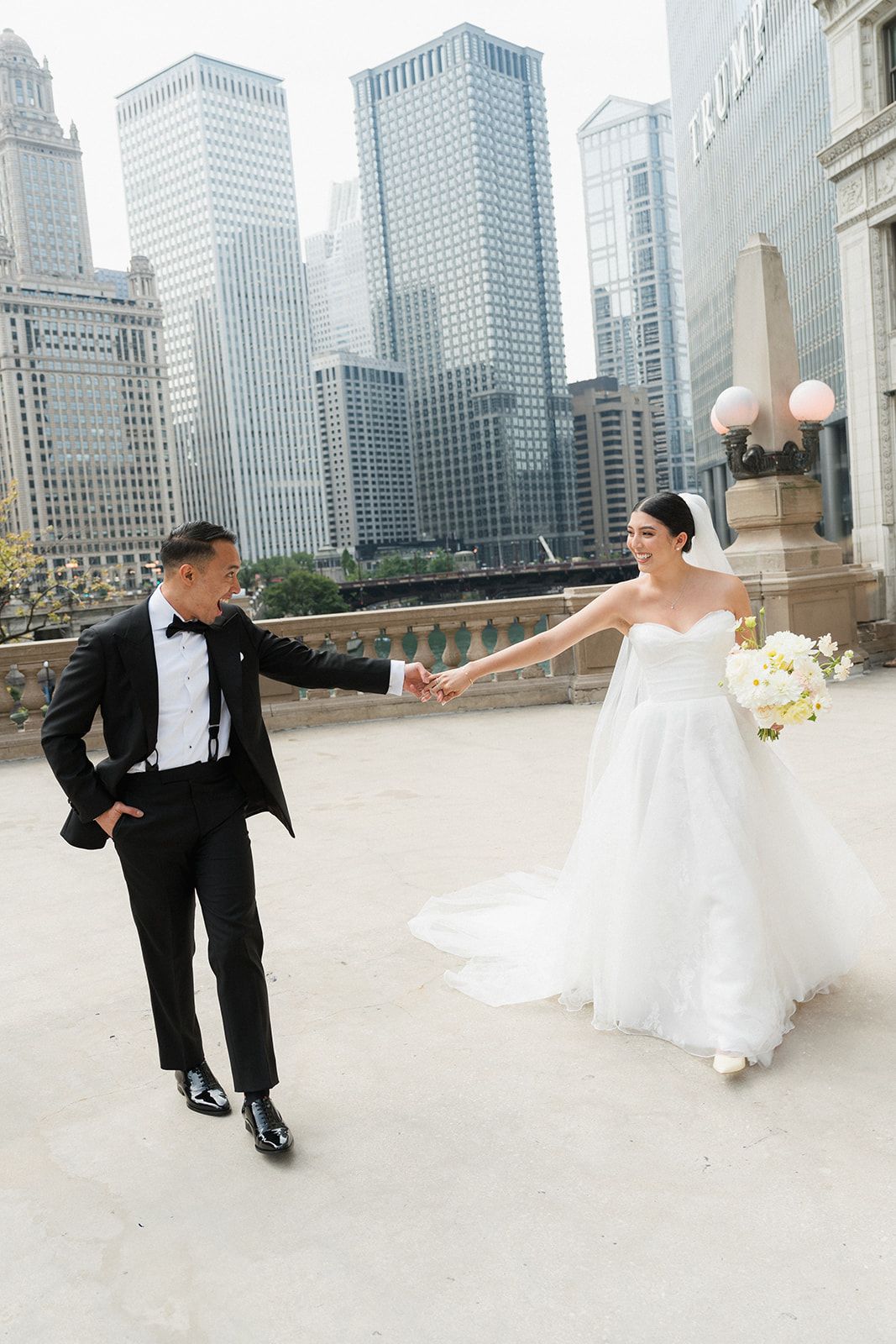 Bride and groom hold hands on rooftop terrace with Chicago city skyline skyscrapers in the background.