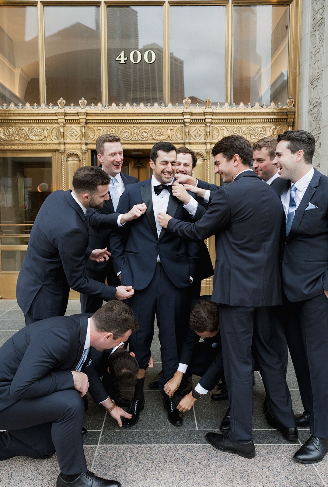 Groomsmen in navy suits celebrating with the groom outside a grand building entrance.
