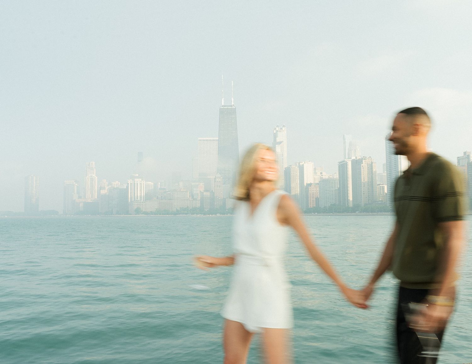 Blurred motion photo of couple holding hands walking along Chicago lakefront with city skyline.