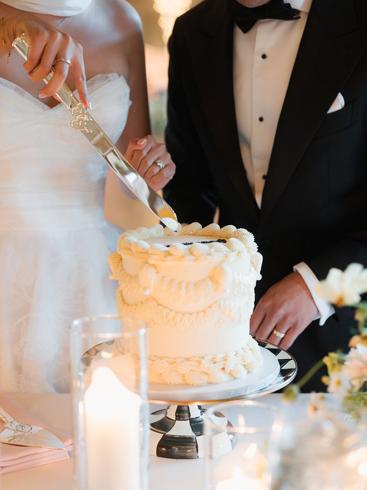 Bride and groom cutting a white tiered wedding cake decorated with elegant piped frosting details at their reception.