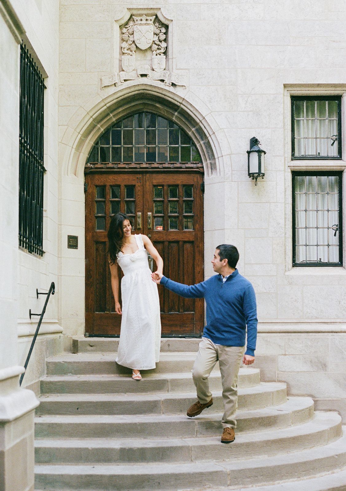 Couple holding hands on stone steps of gothic building with ornate wooden arched doorway.
