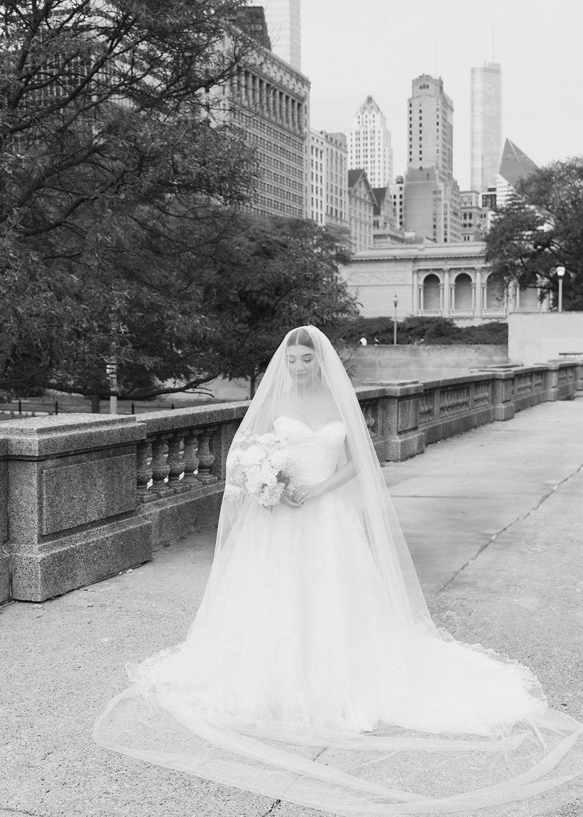 Black and white bridal portrait with cathedral veil and bouquet against urban city skyline backdrop.