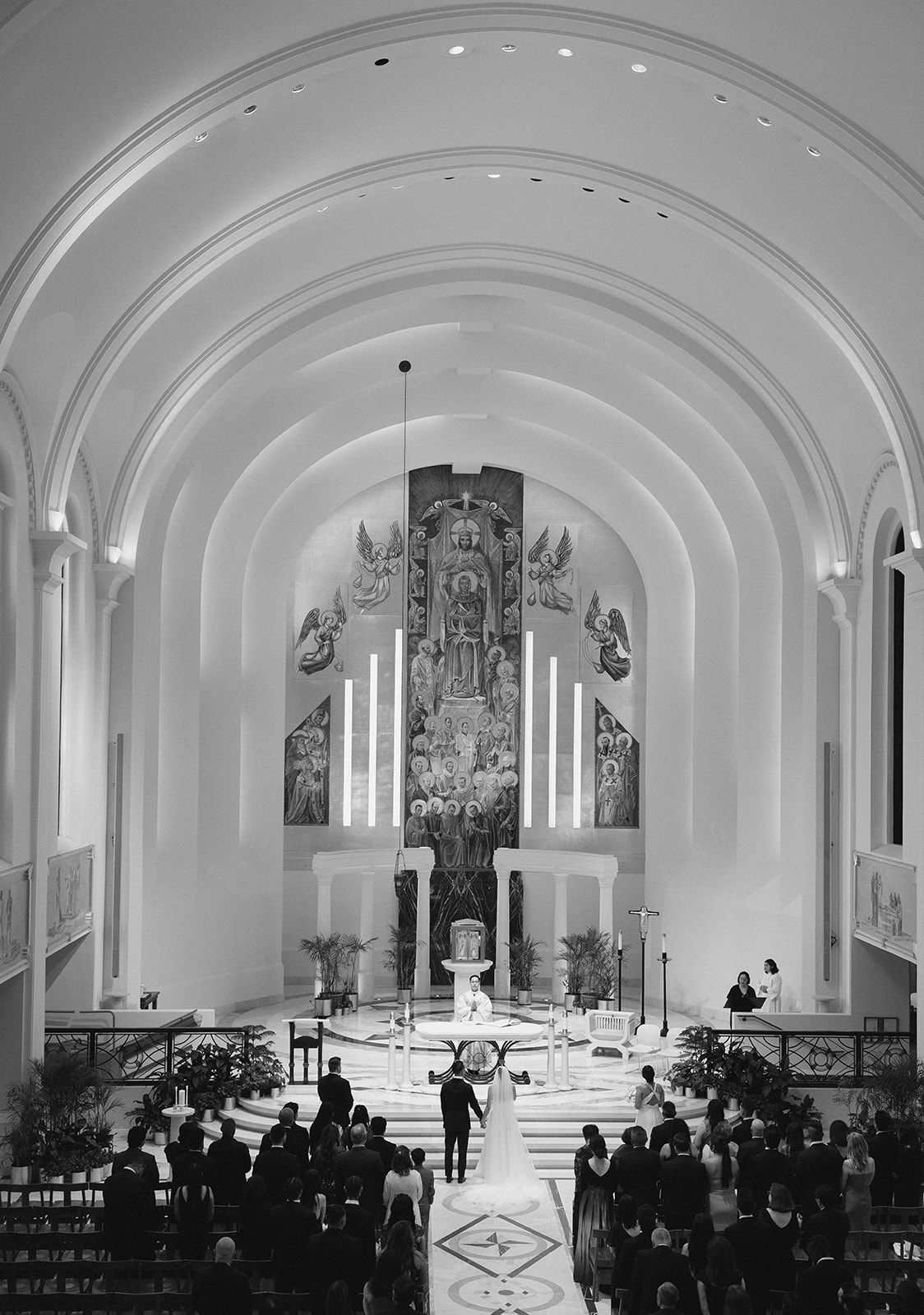 Black and white photo of a wedding ceremony inside a grand cathedral with arched ceilings and ornate altar.