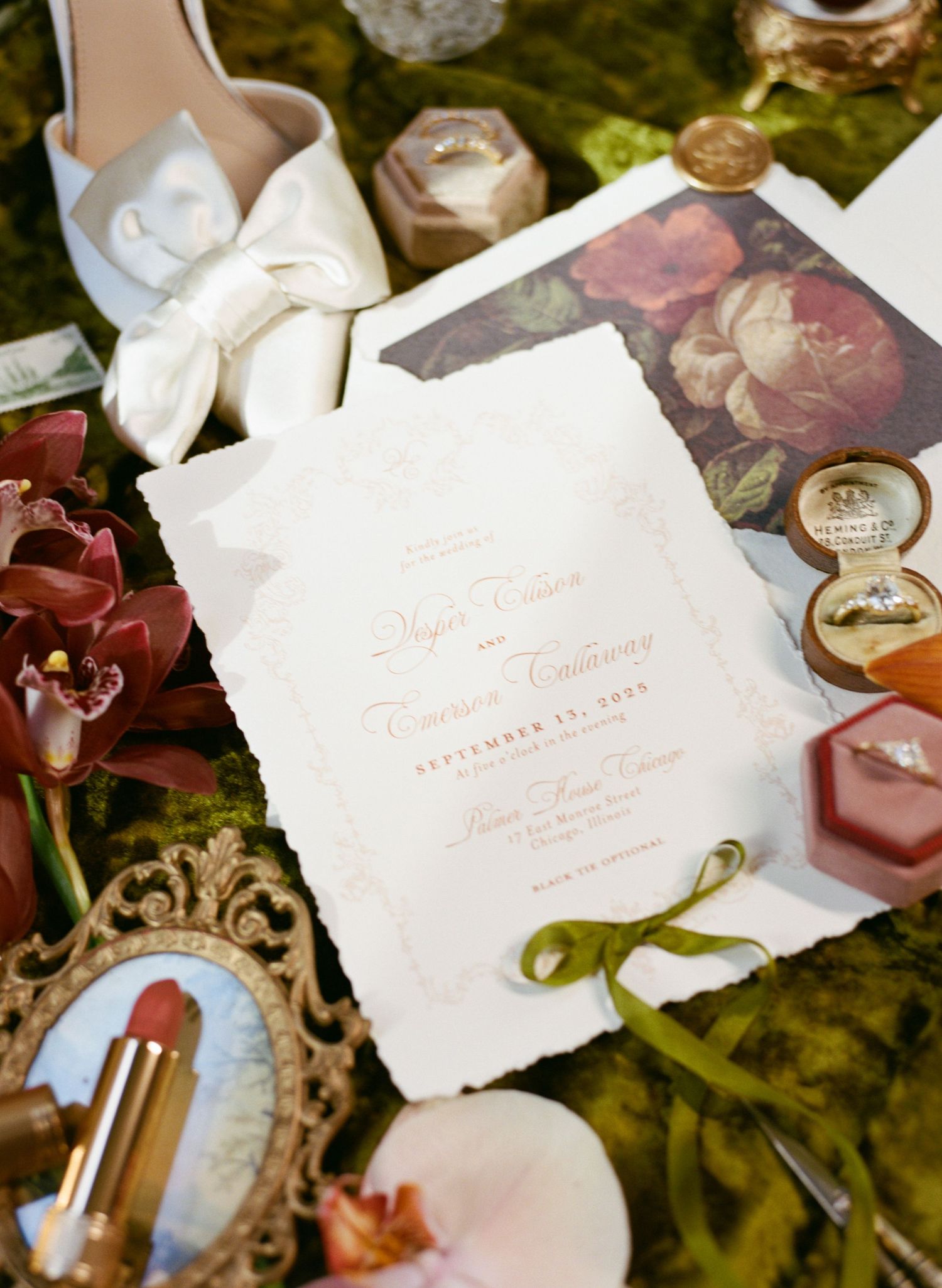 Elegant wedding invitation flatlay with rings, floral envelope liner, bridal heels, and vintage mirrors on green velvet.
