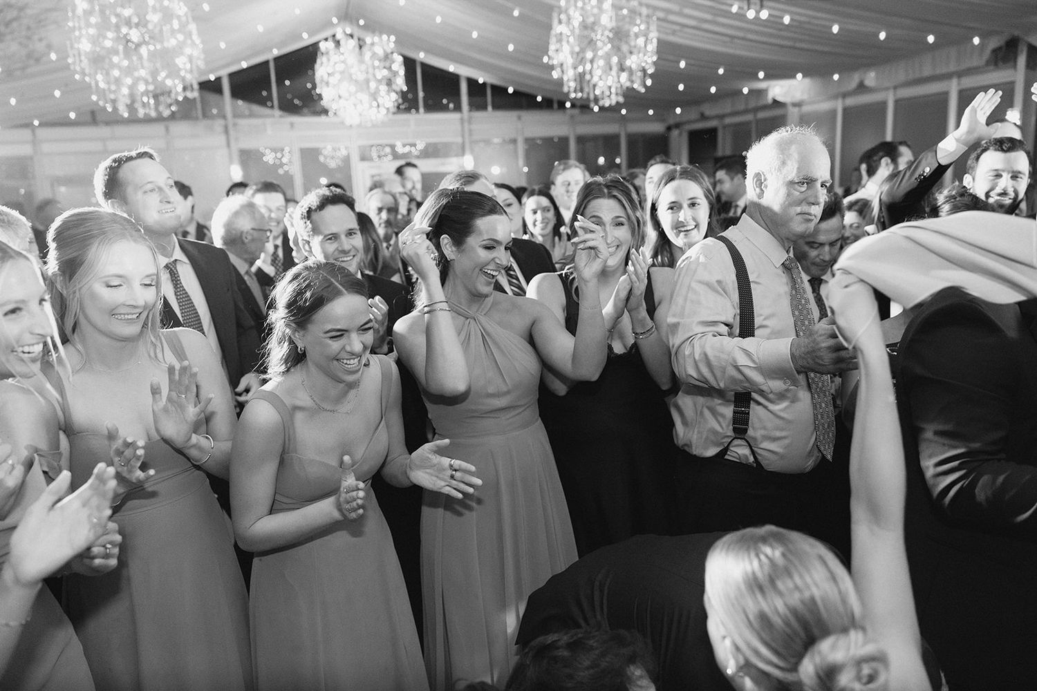Black and white photo of wedding guests and bridesmaids dancing joyfully at elegant tented reception.