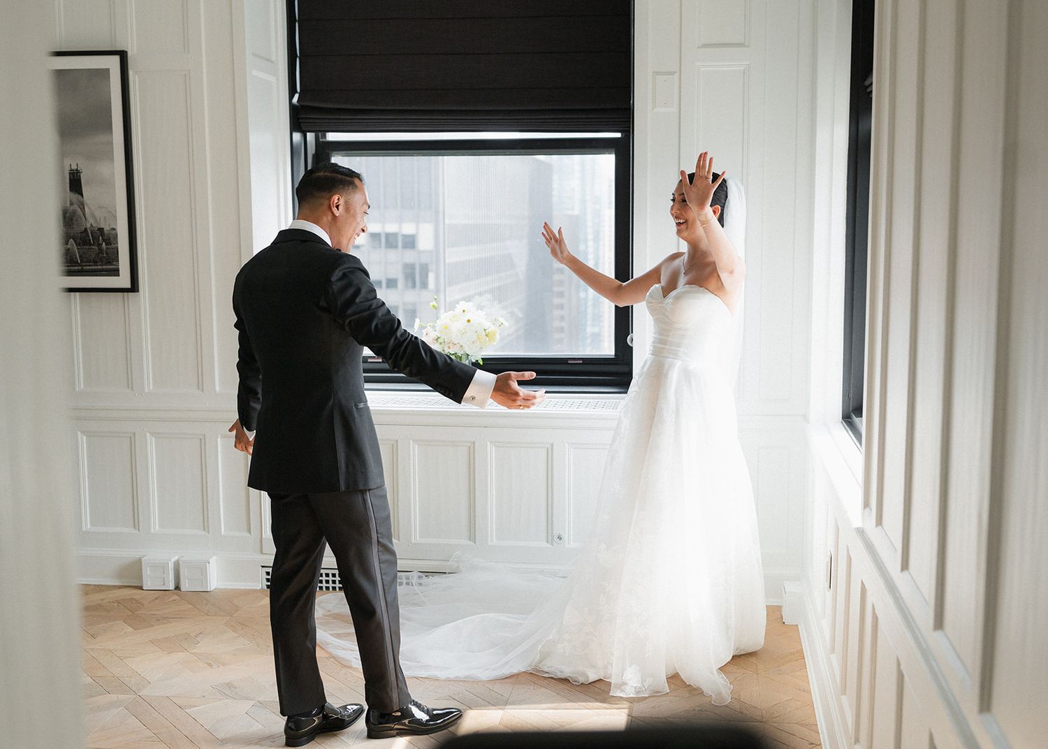 Bride and groom sharing a first look moment by large windows in an elegant white room.
