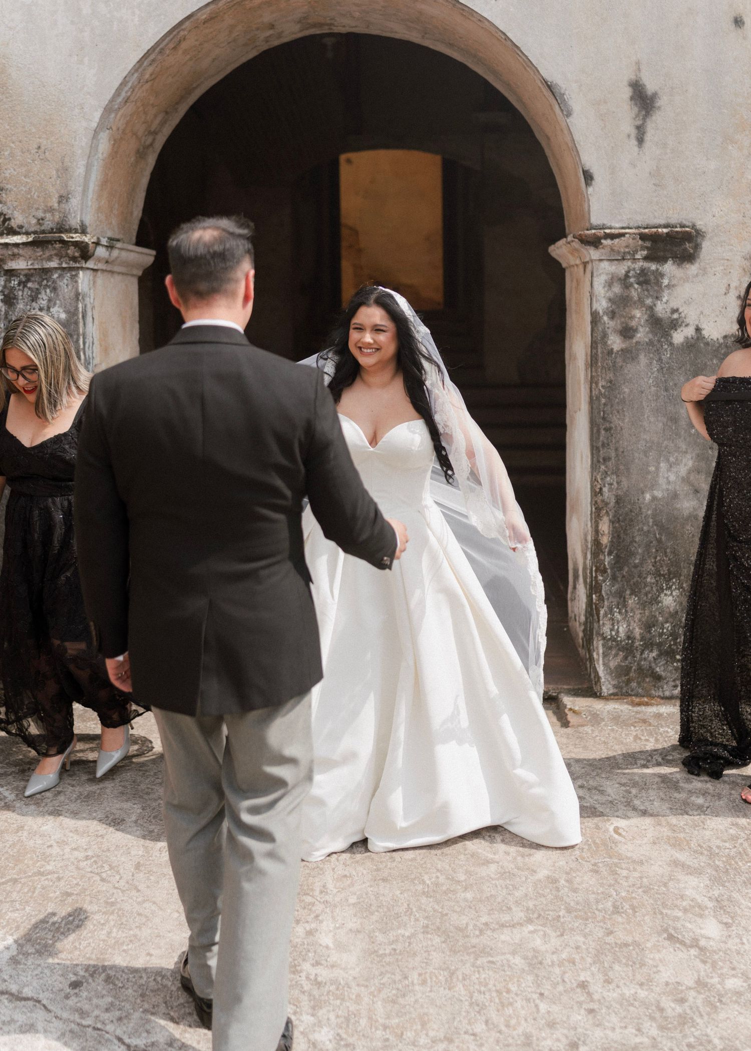 Bride in white ball gown and veil shares first look moment with groom in black suit at stone arch venue.