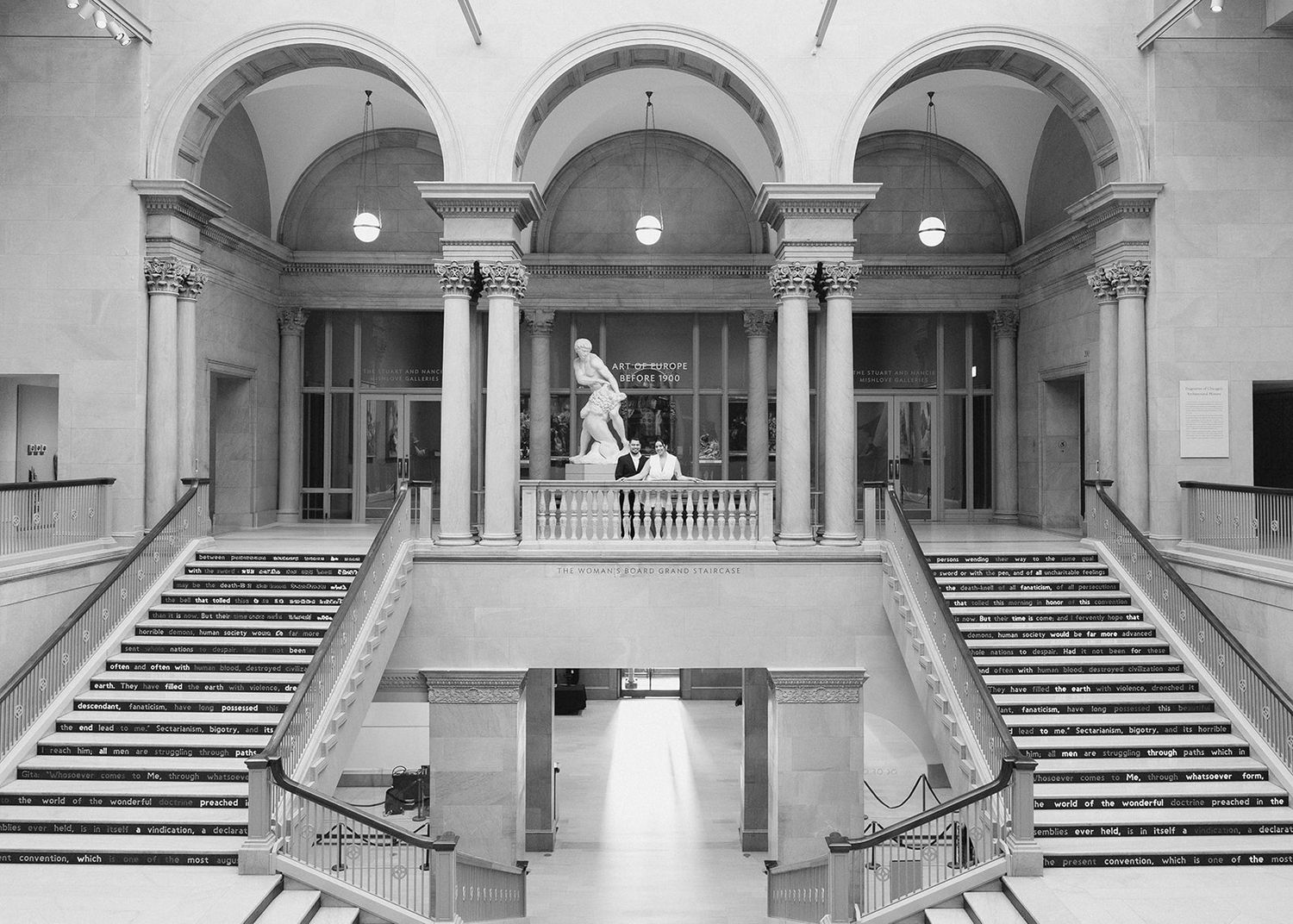 Grand neoclassical museum interior featuring marble staircases, tall columns, and a central sculpture.
