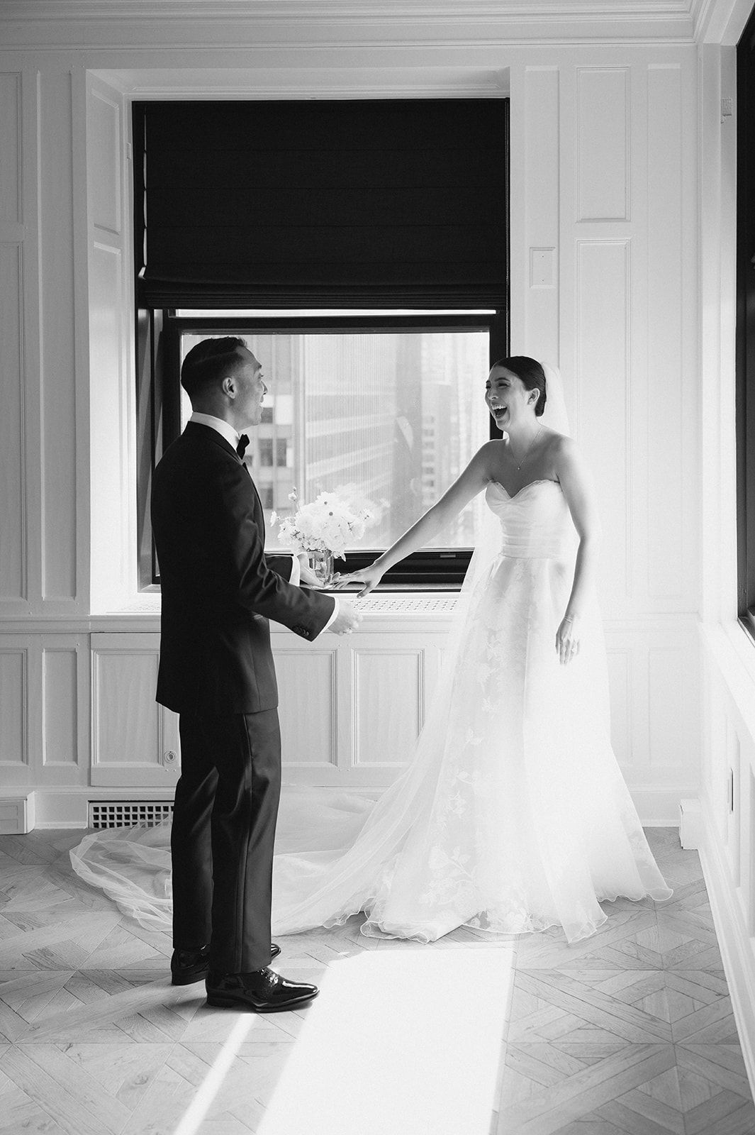Black and white photo of bride and groom sharing first look moment in elegant white paneled room by window.
