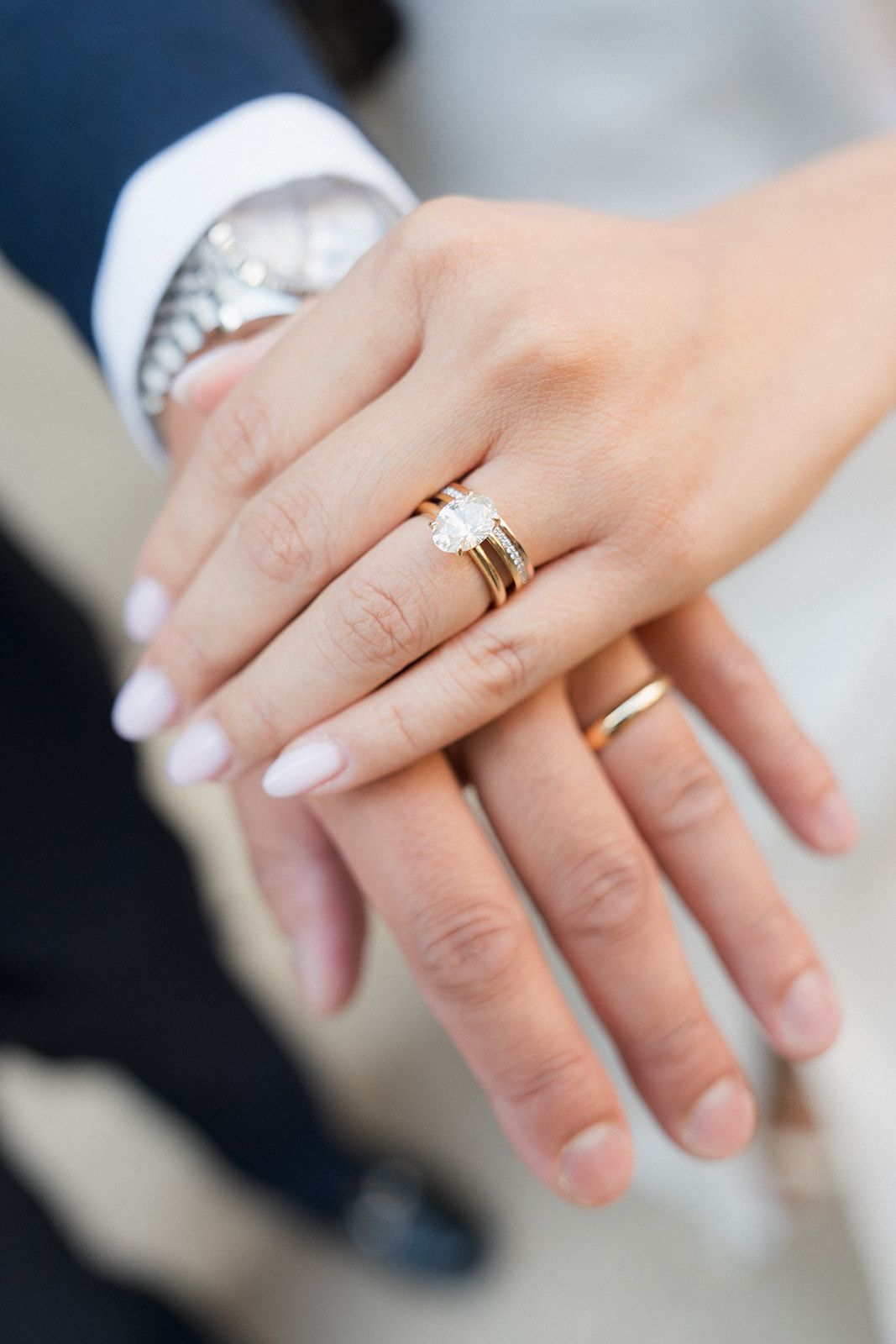 Close-up of newlyweds hands showcasing a gold diamond engagement ring and matching wedding bands.