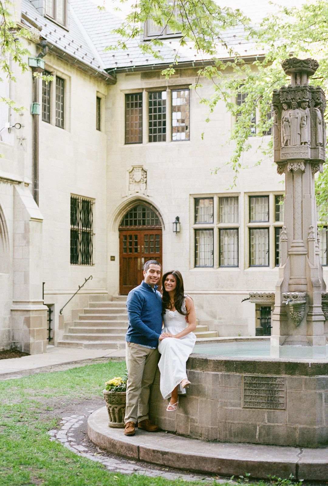 Couple posing together at a stone fountain outside a historic building.