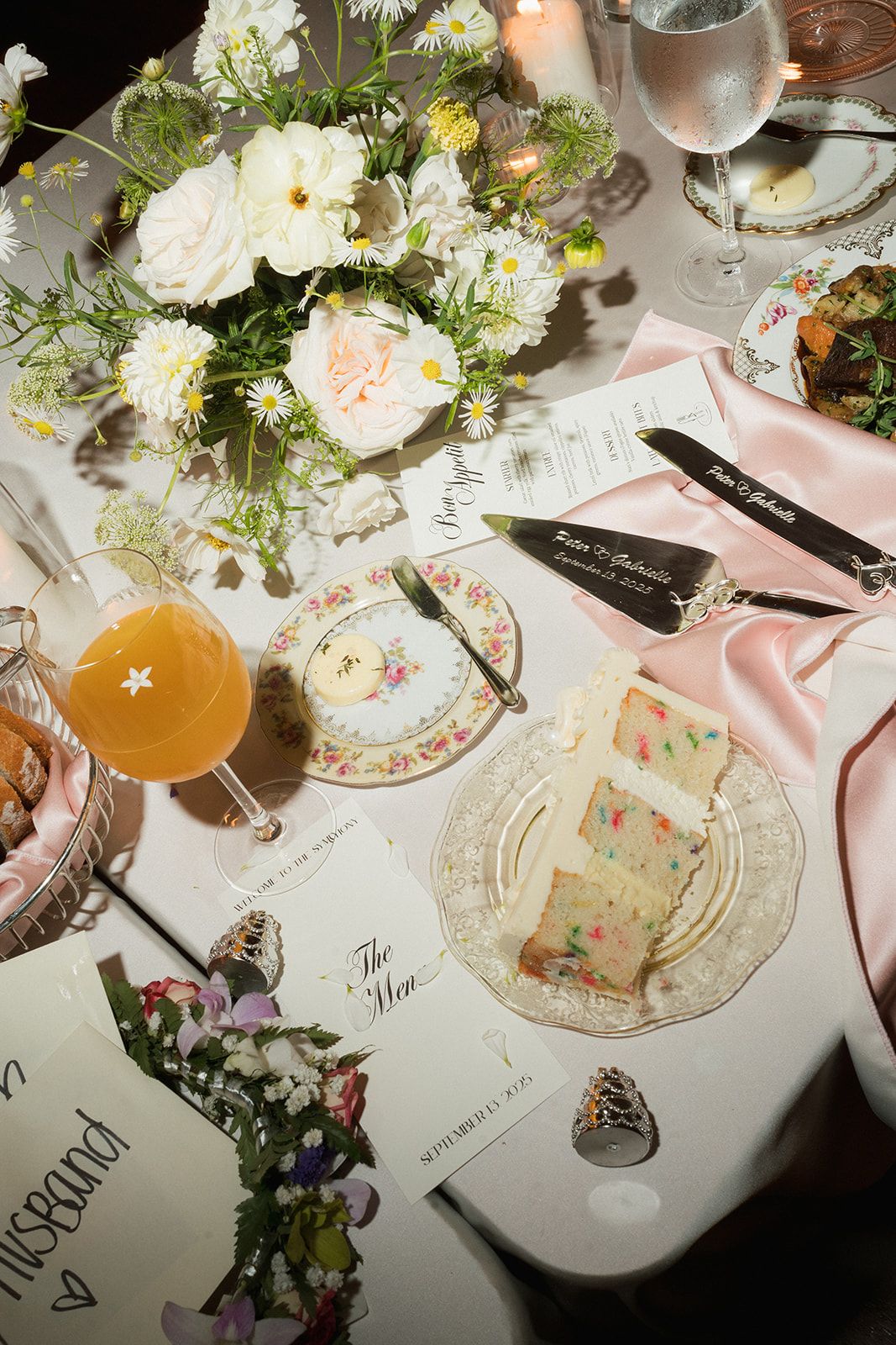 Elegant wedding tablescape with floral centerpiece, funfetti cake slice, pink napkins, and vintage china.