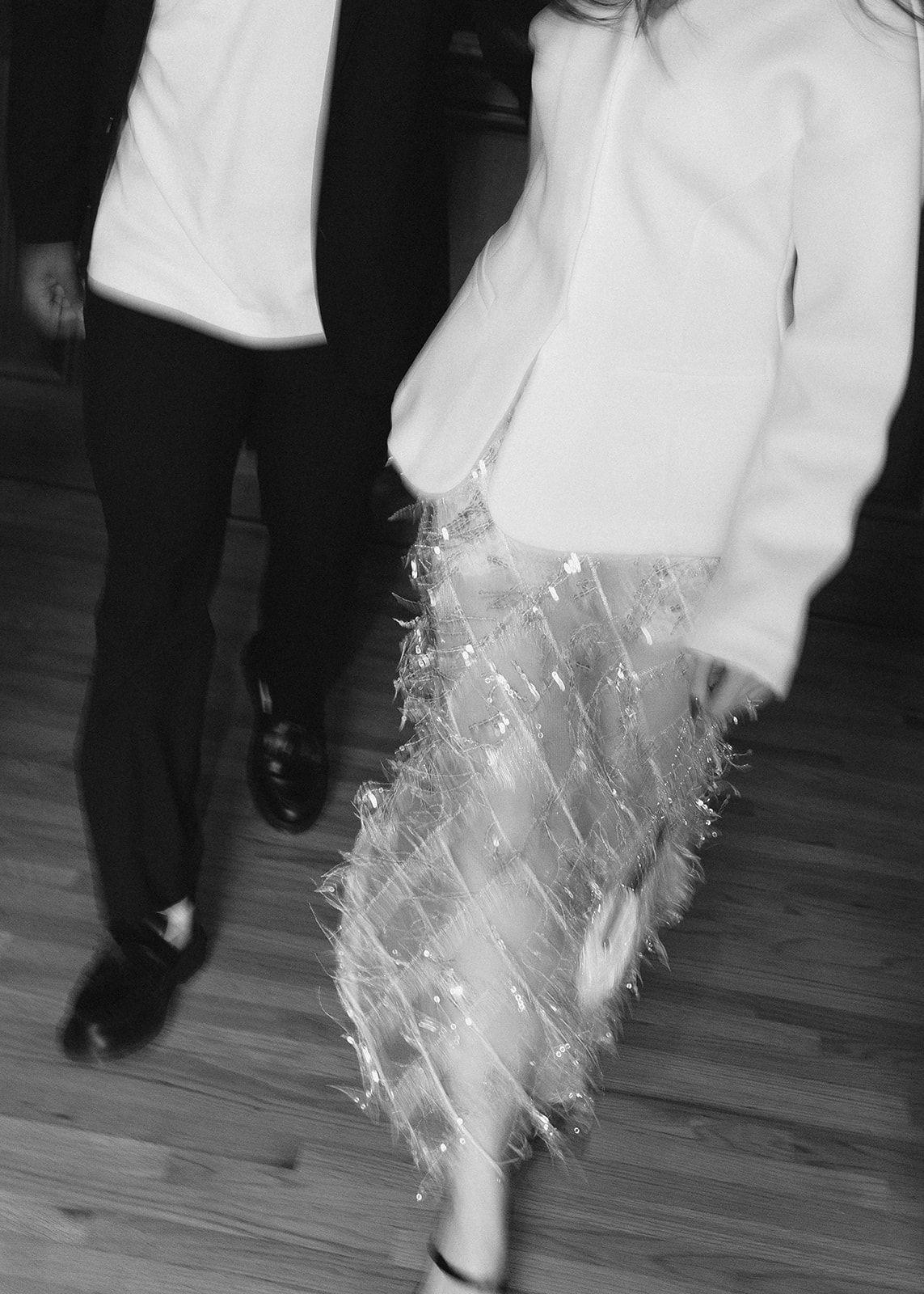 Black and white photo of couple walking on hardwood floor, woman in sparkly tulle skirt.