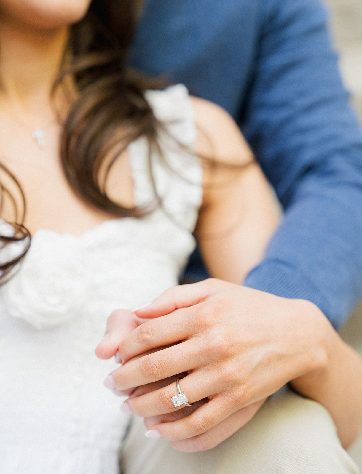 Close-up of woman's hand showing a square diamond engagement ring while sitting with her partner.