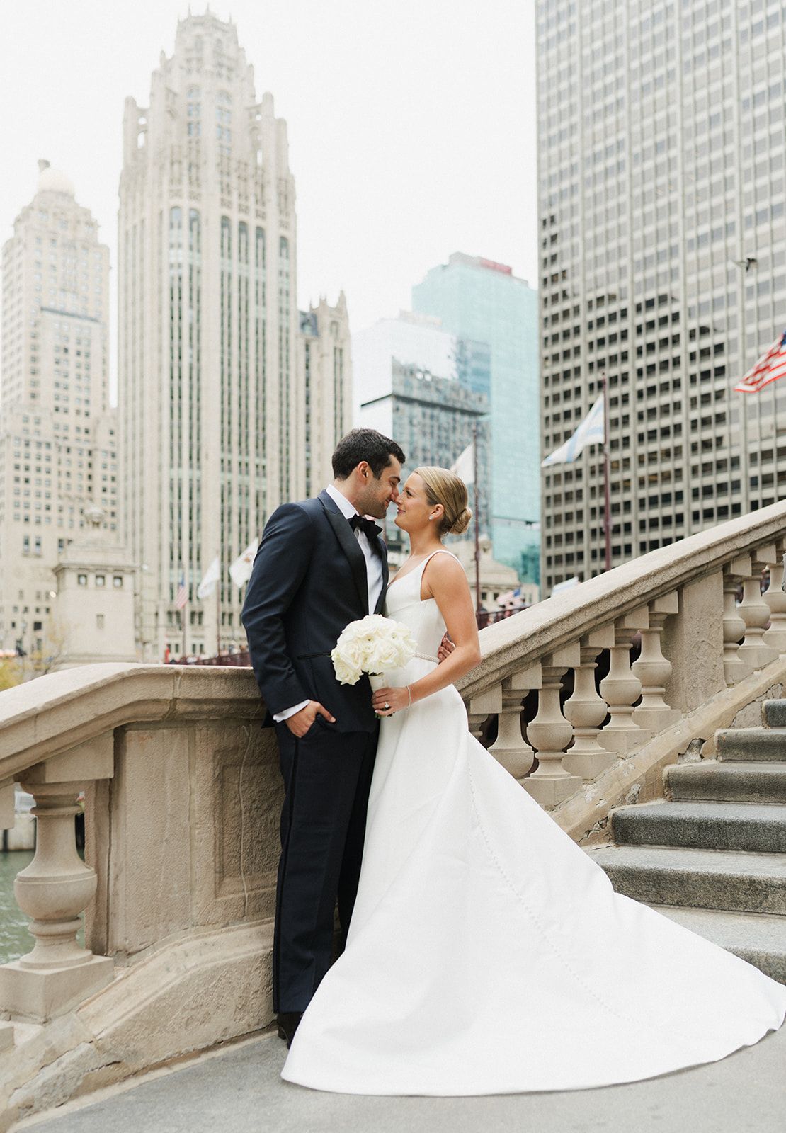 Bride and groom share romantic moment on stone steps with Chicago skyline and Tribune Tower backdrop.