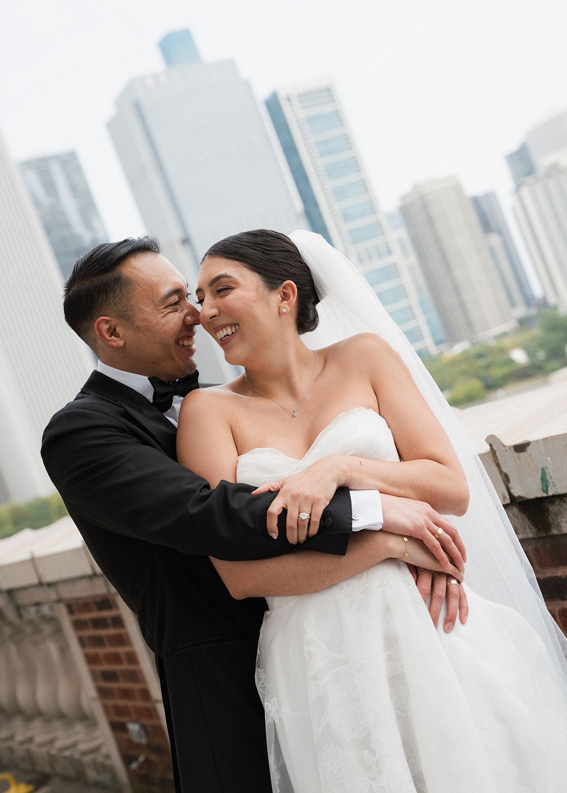 Smiling bride and groom embrace on rooftop with Chicago city skyline backdrop on their wedding day.
