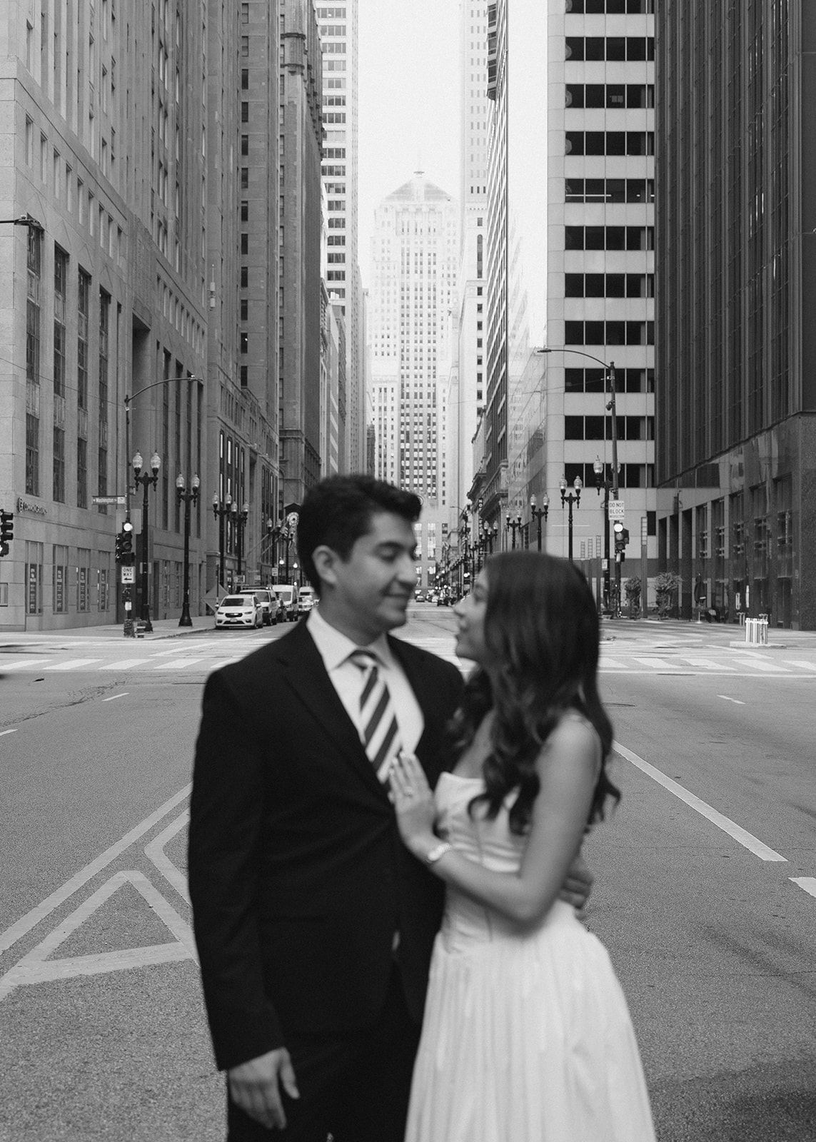 Black and white photo of a couple embracing on an empty city street with skyscrapers.
