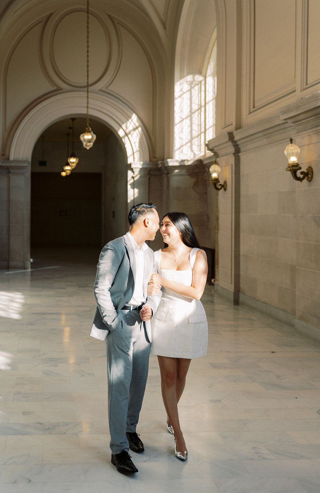 Couple in elegant attire sharing a romantic moment inside a grand marble hall with arched ceilings.