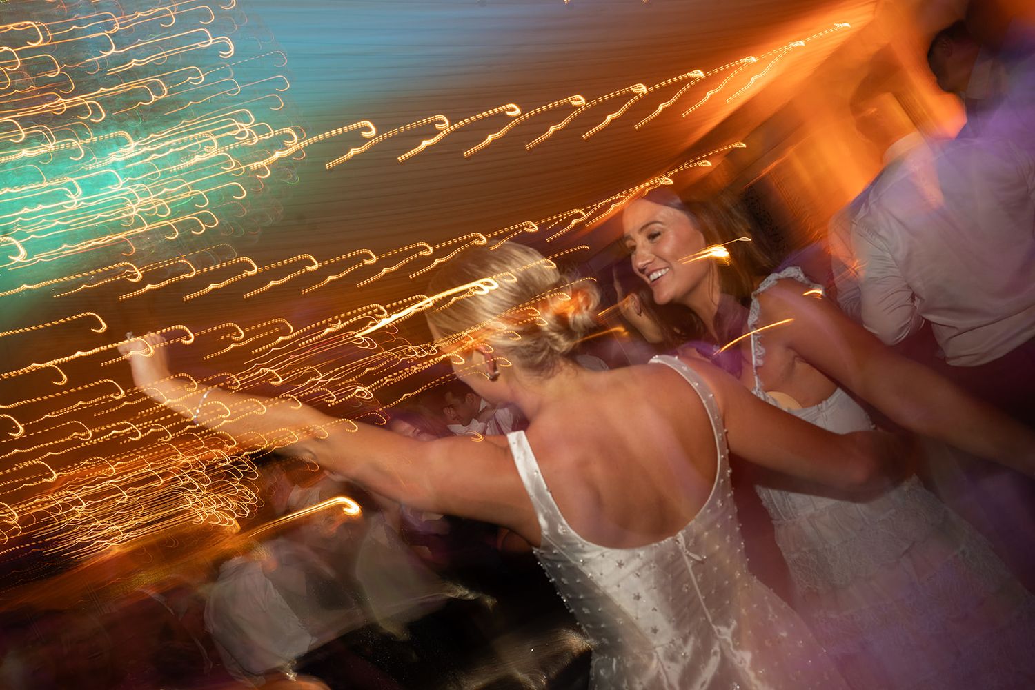 Blurred motion photo of a bride in a white dress dancing joyfully at a wedding reception with colorful lights.