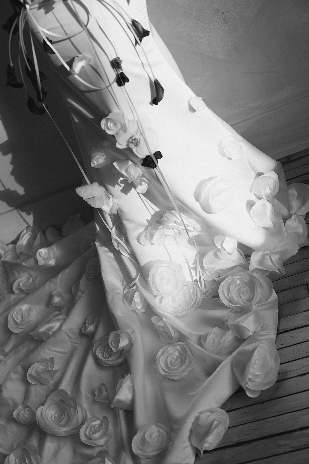 Black and white photo of an elegant wedding gown adorned with fabric roses and floral appliques hanging on display.