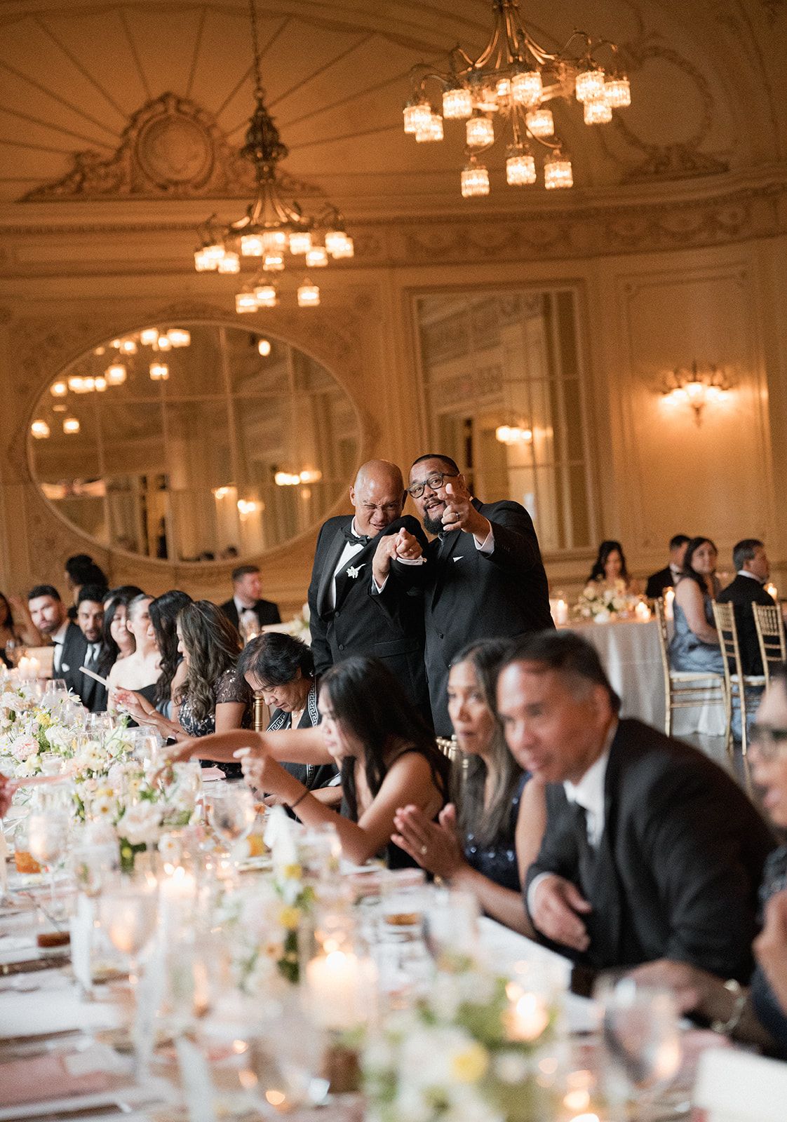 Guests laughing and celebrating at a luxurious wedding reception in an ornate gold ballroom.