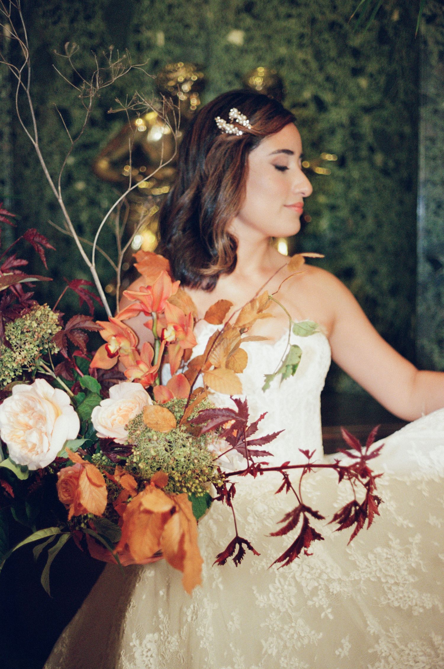 Bride in lace gown holds lush autumn bouquet of orange, burgundy, and white blooms with foliage.