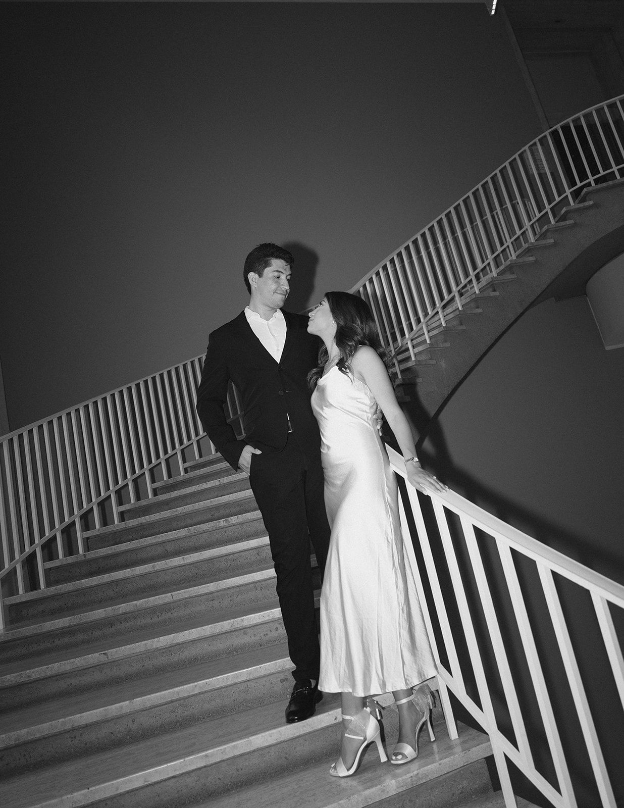Black and white photo of couple in formal wear sharing a romantic moment on a grand staircase.
