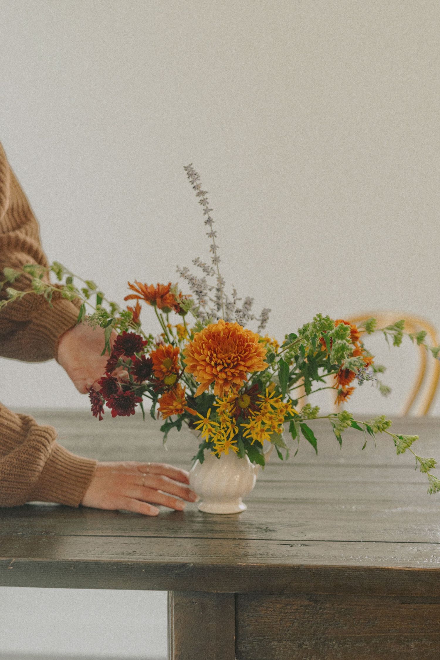 Hands place a bouquet of autumn wildflowers on a wooden table during a styled, fine art, nature-inspired portrait session.