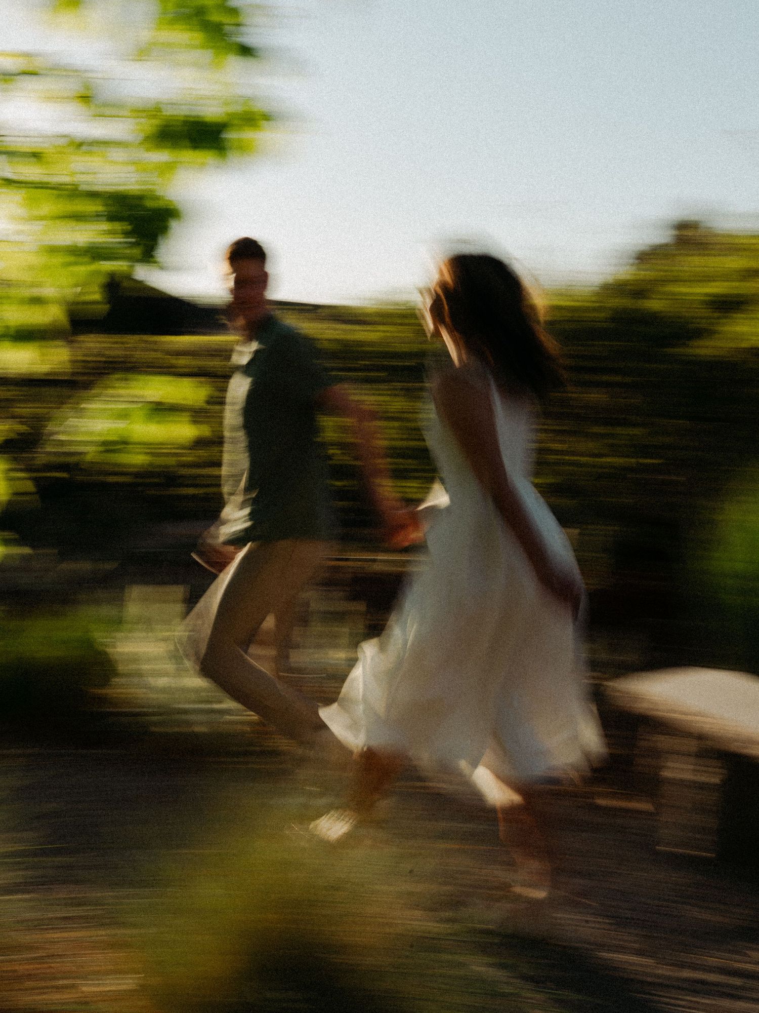 A couple dances joyfully outdoors in a sun-drenched garden, captured with intentional motion blur.