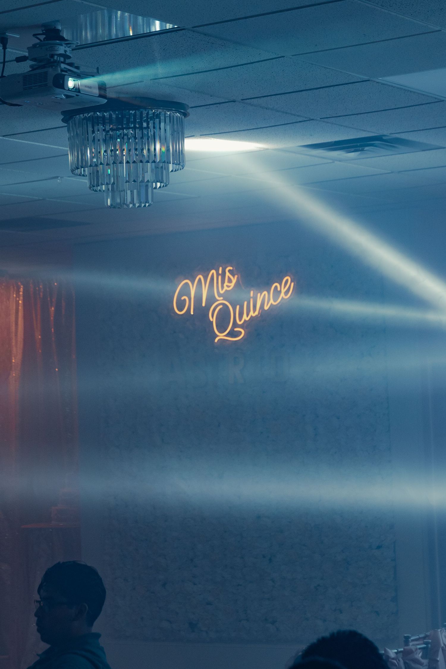 Neon Mis Quince sign glowing on a wall with dramatic light beams at a quinceañera celebration.