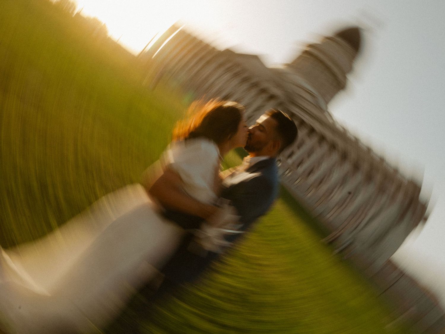 Couple sharing a romantic kiss near the Leaning Tower of Pisa with a dreamy spin blur effect.