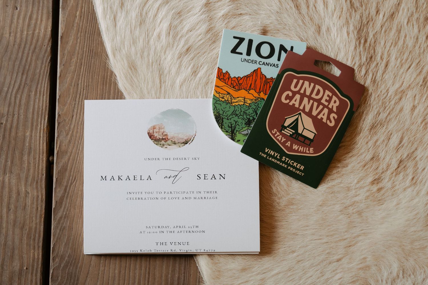Wedding invitation for Makaila and Sean displayed with Zion National Park and Under Canvas keychains on a fur surface.