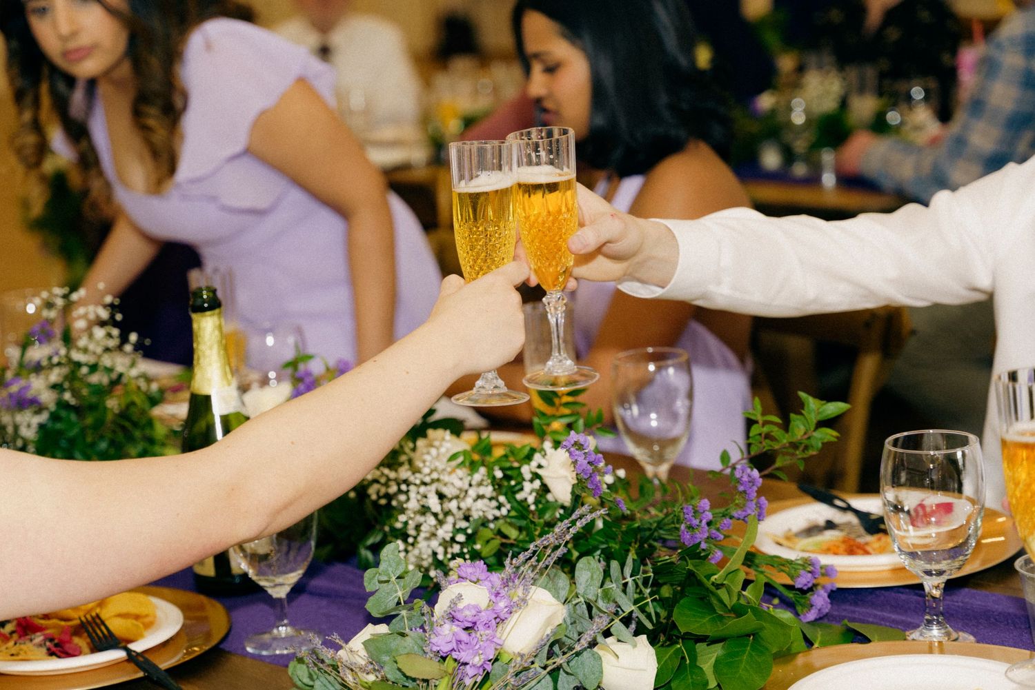 Guests clinking champagne glasses over floral centerpiece at elegant wedding reception dinner.