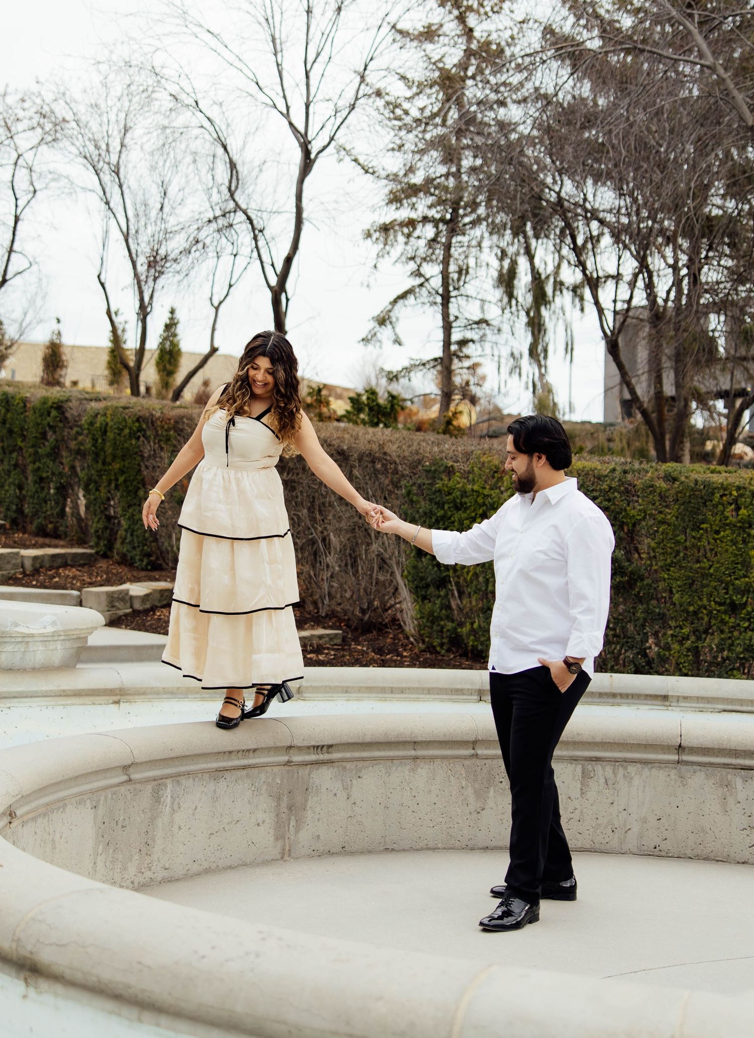 Couple holding hands during outdoor engagement photo session at decorative stone fountain.
