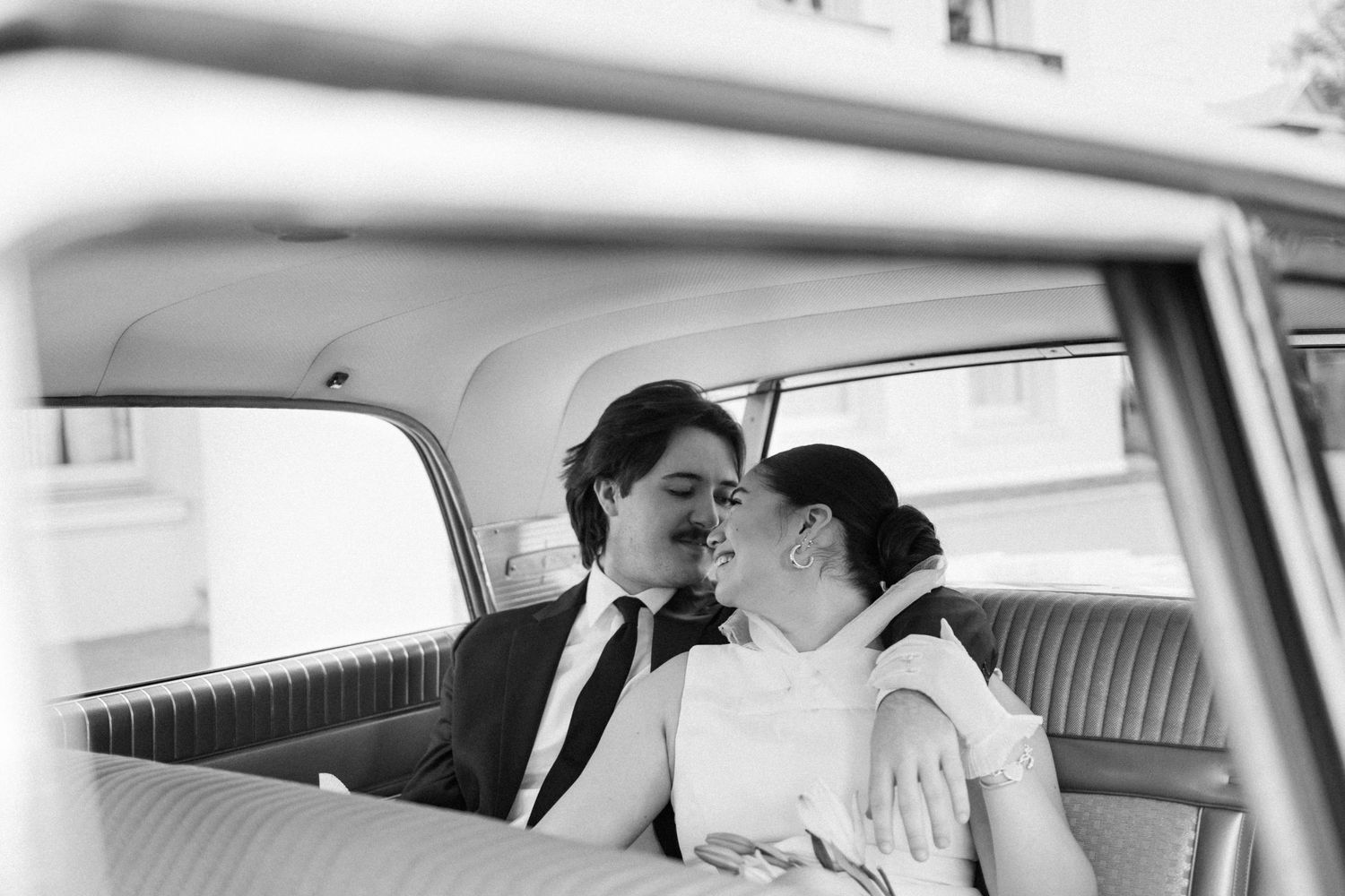 Black and white photo of a bride and groom sharing a kiss in a vintage car.