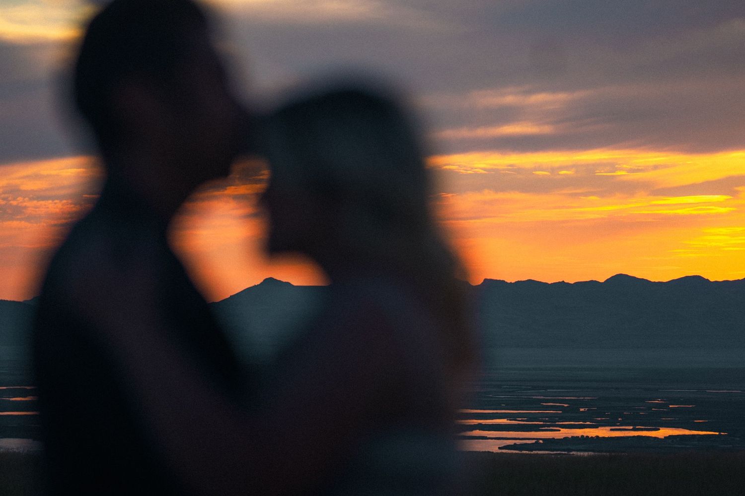 A blurred silhouette of a couple embracing against a vibrant orange sunset over water.